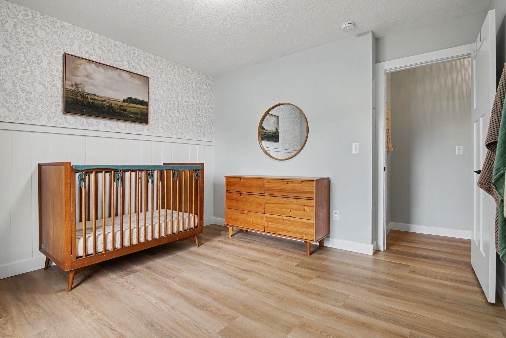 Interior room featuring wood-finish flooring, light gray painted walls, and a feature wall with white wainscoting and patterned wallpaper