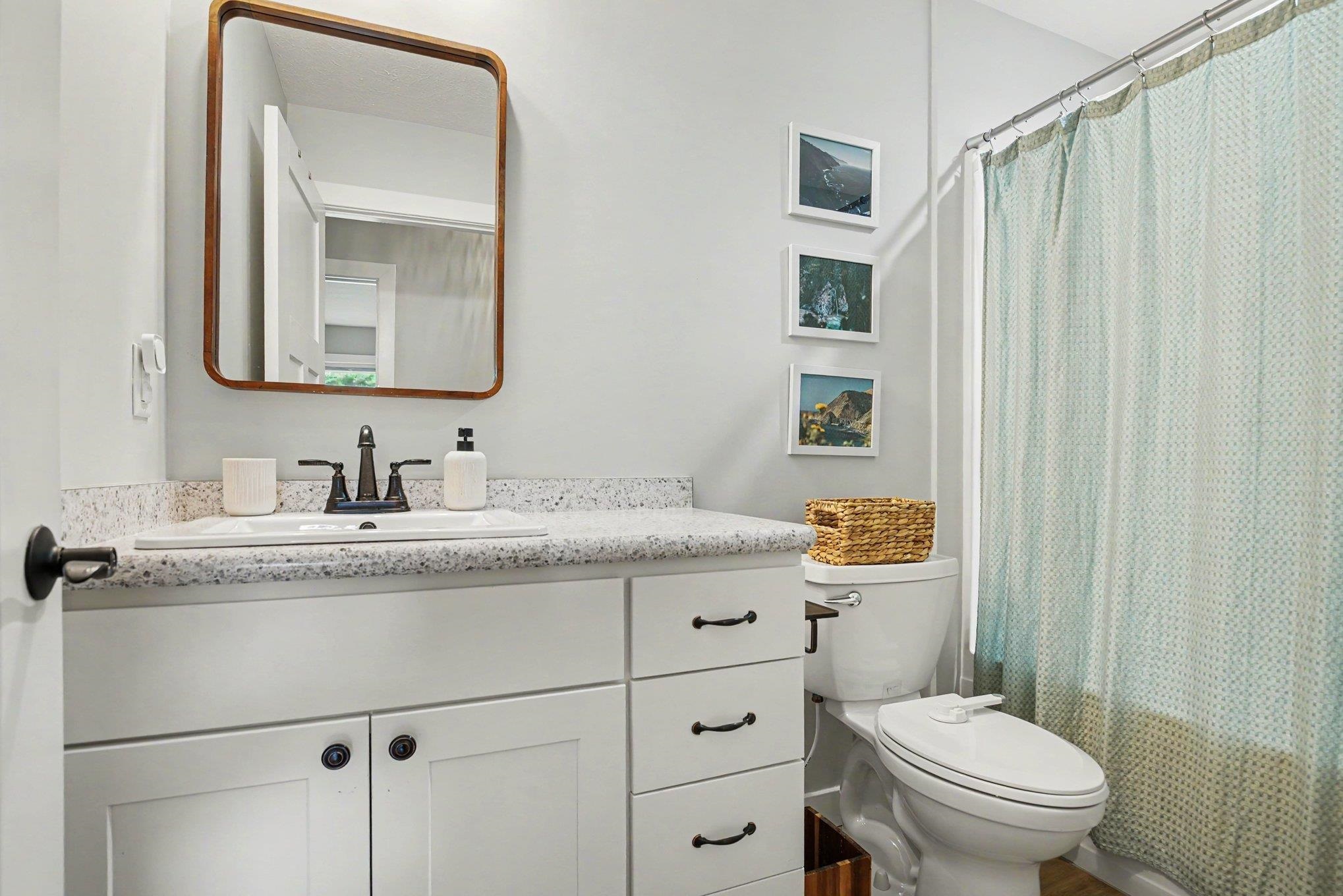 Bathroom featuring a white vanity with dark hardware, a speckled countertop, an undermount sink with a dark-finish faucet, and a wall-mounted mirror