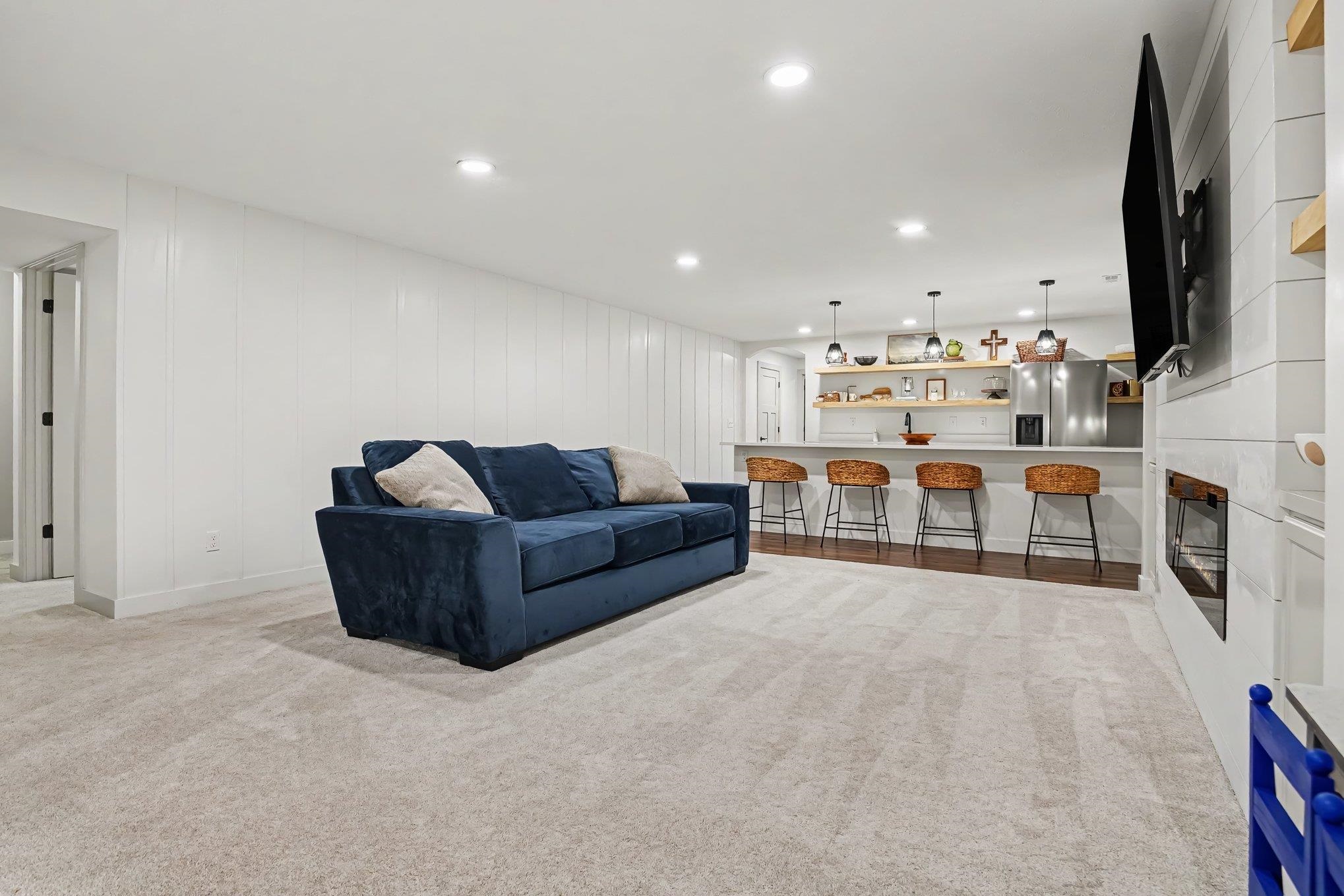Spacious open-concept room featuring light-toned carpeting, white shiplap-style wall paneling, and recessed lighting
