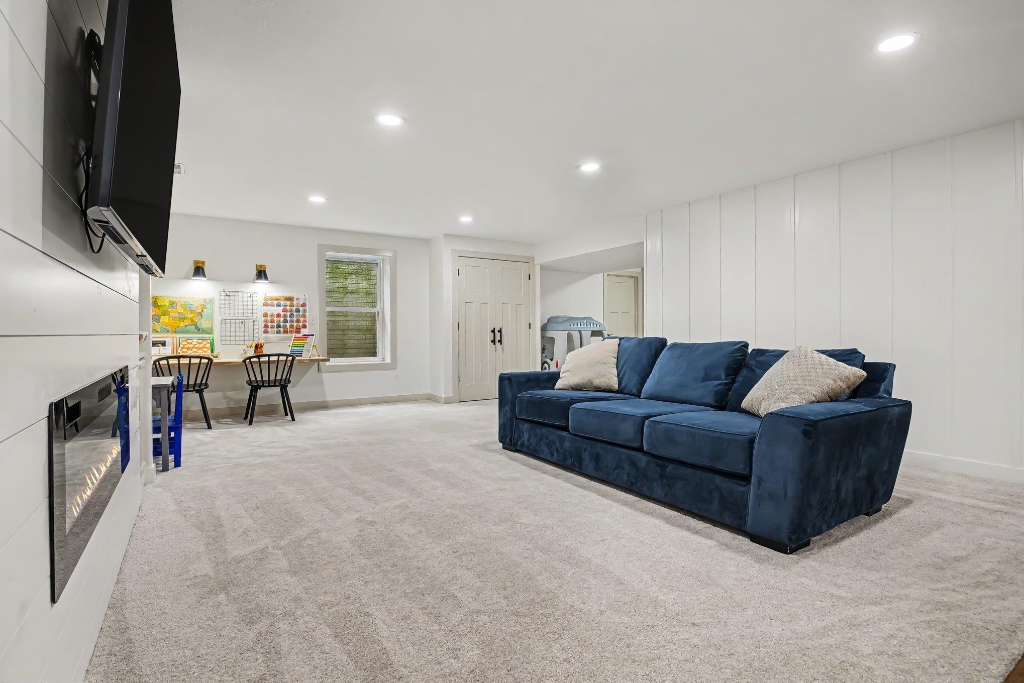 Finished basement space featuring recessed lighting, light-toned carpeting, a built-in electric fireplace with shiplap-style surround, a window with natural light, and paneled walls