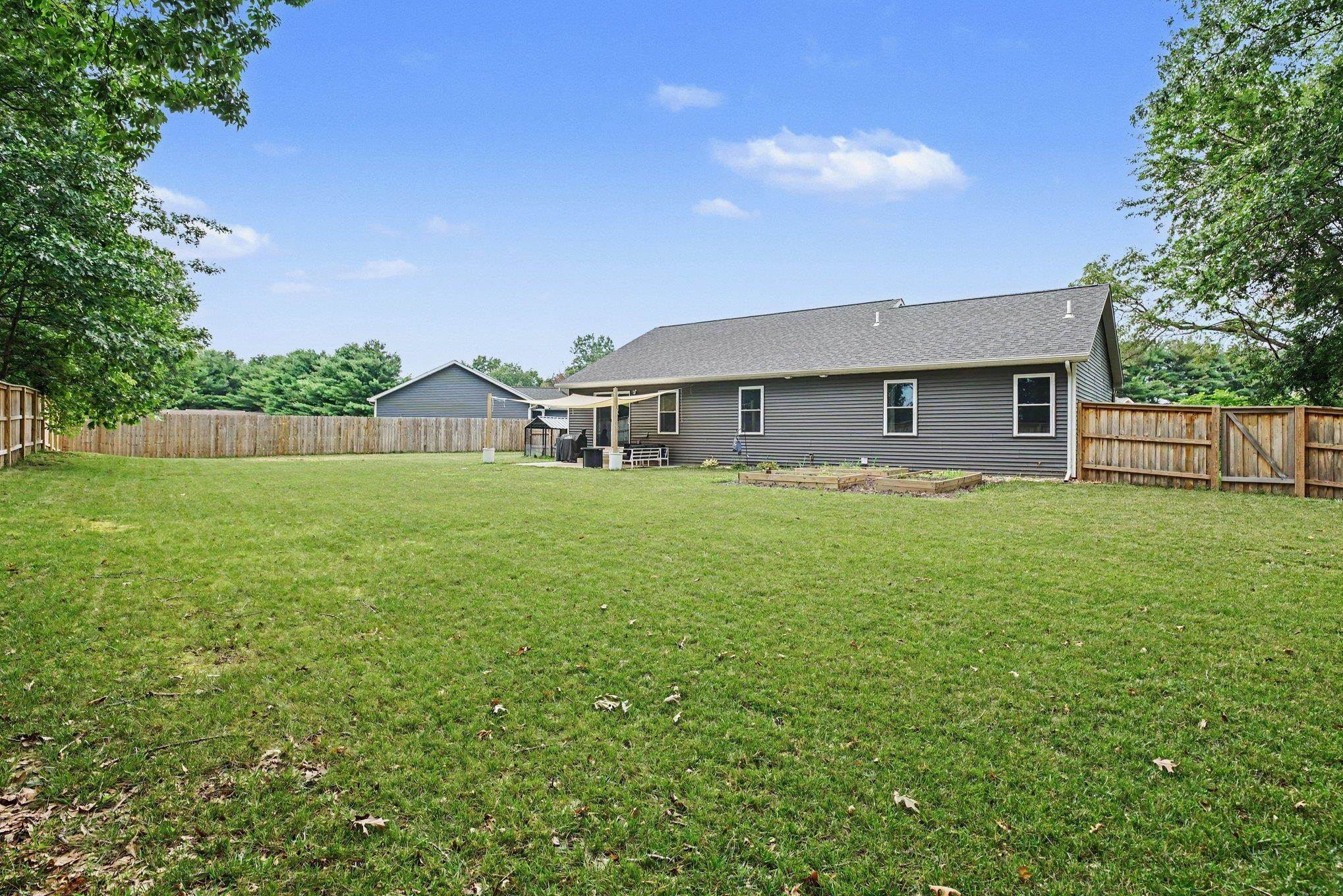 Expansive backyard featuring a manicured lawn, full perimeter wood fencing, and a covered patio area