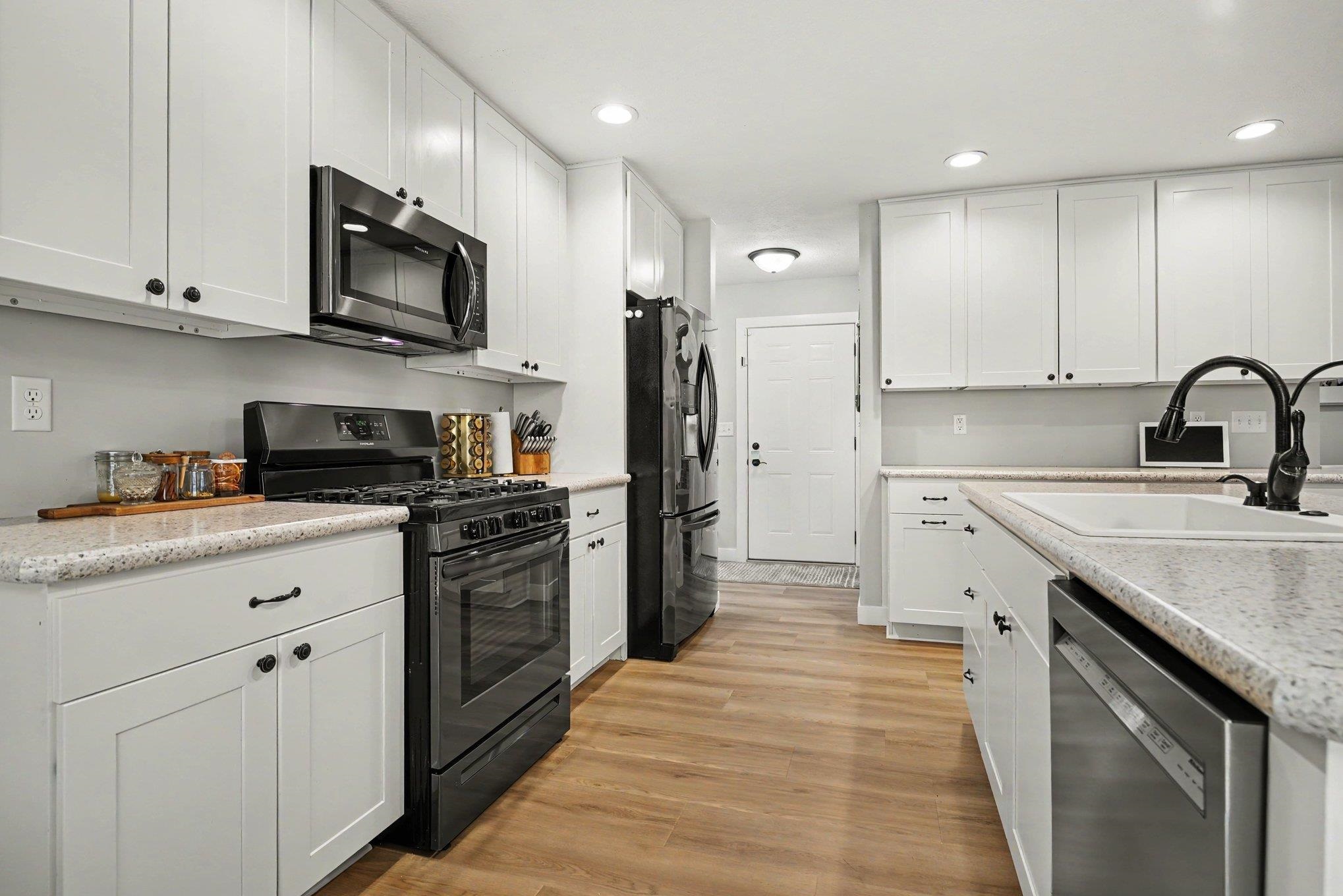 Bright kitchen featuring white shaker cabinetry, light-toned countertops, wood-finish flooring, recessed lighting, and stainless steel appliances