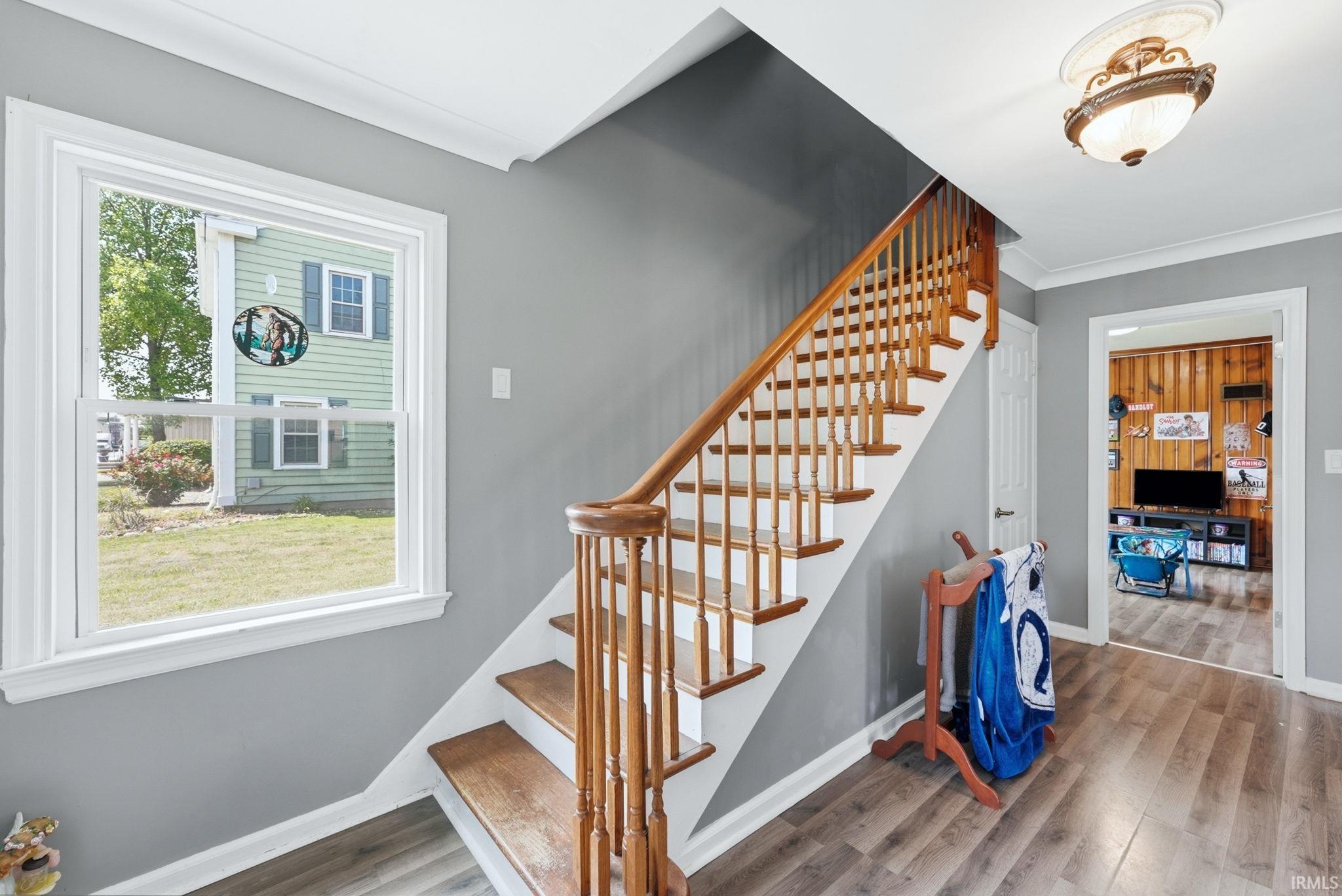 Inviting entryway featuring wood-finish flooring, a staircase with wood treads and banister, white trim, and a window providing natural light
