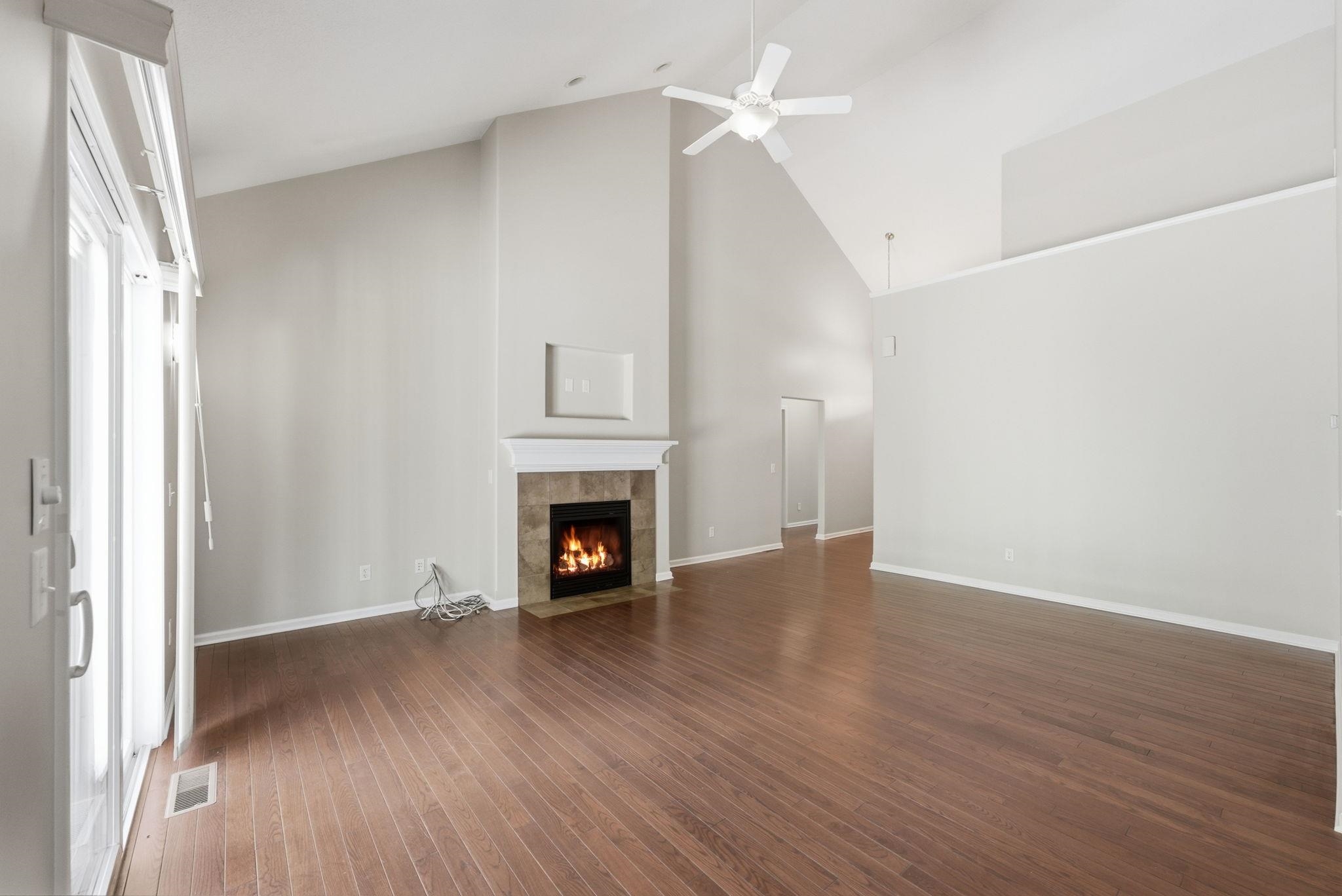 Spacious living area featuring vaulted ceilings, wood-finish flooring, and a fireplace with a tile surround and mantel