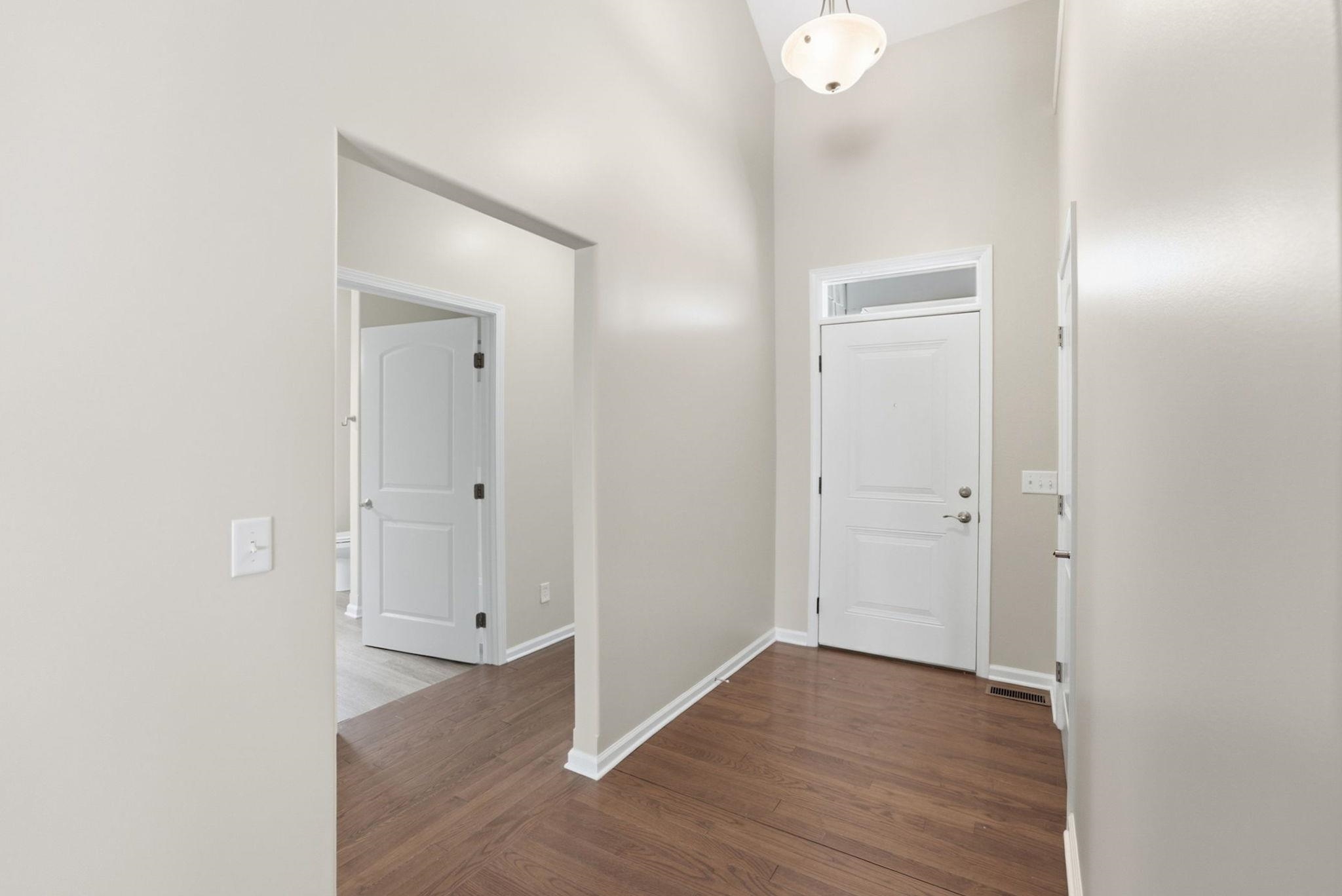 Entryway featuring wood-finish flooring, vaulted ceiling, and a prominent front door with an overhead transom window