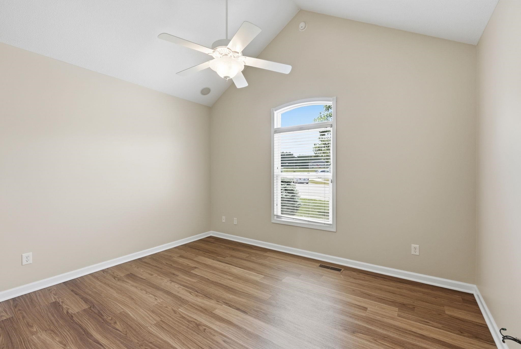 Room featuring a vaulted ceiling with a ceiling fan, wood-finish flooring, and light-toned walls