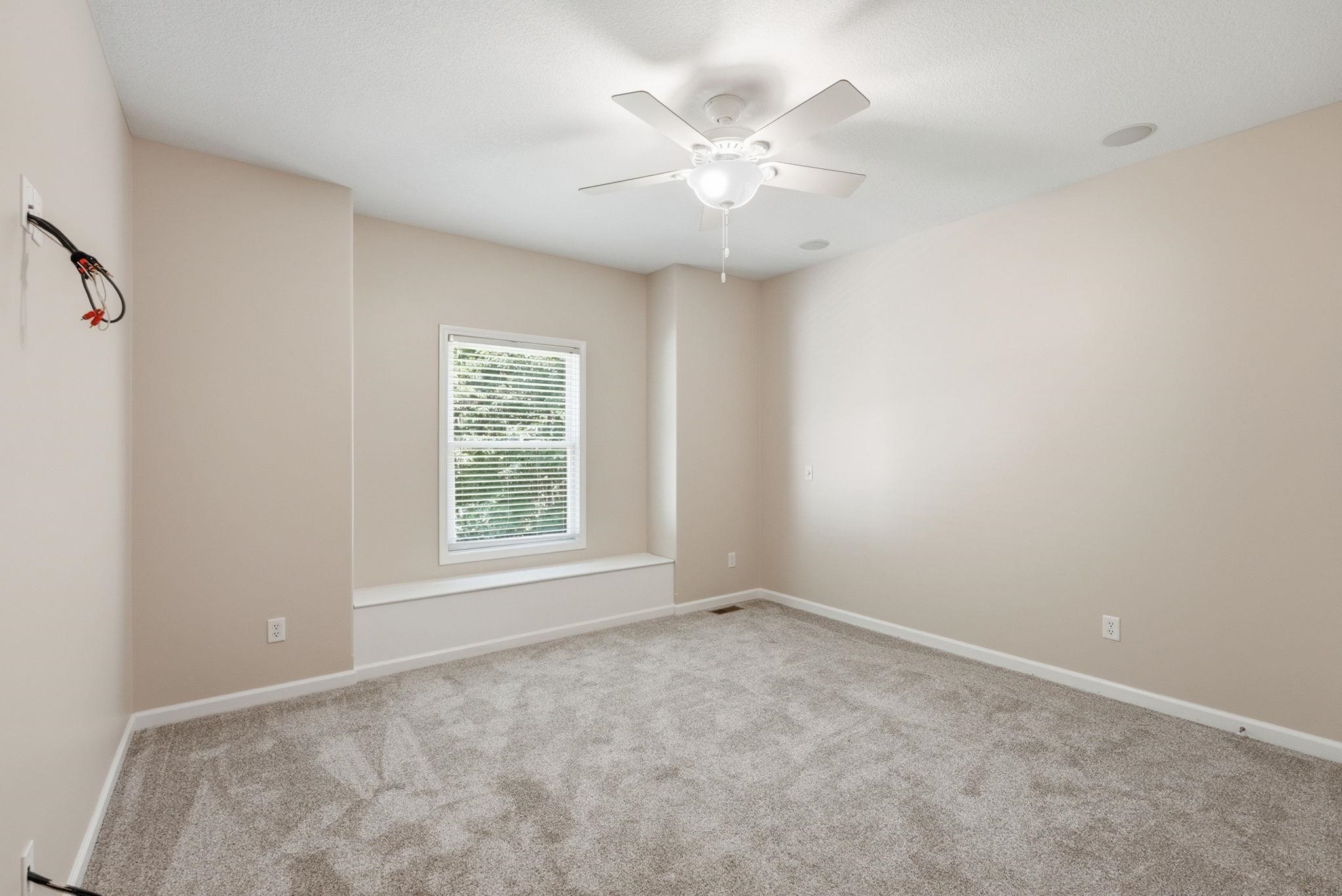 Carpeted interior room featuring a ceiling fan, a window with horizontal blinds, a built-in window bench, and wall-mounted speakers