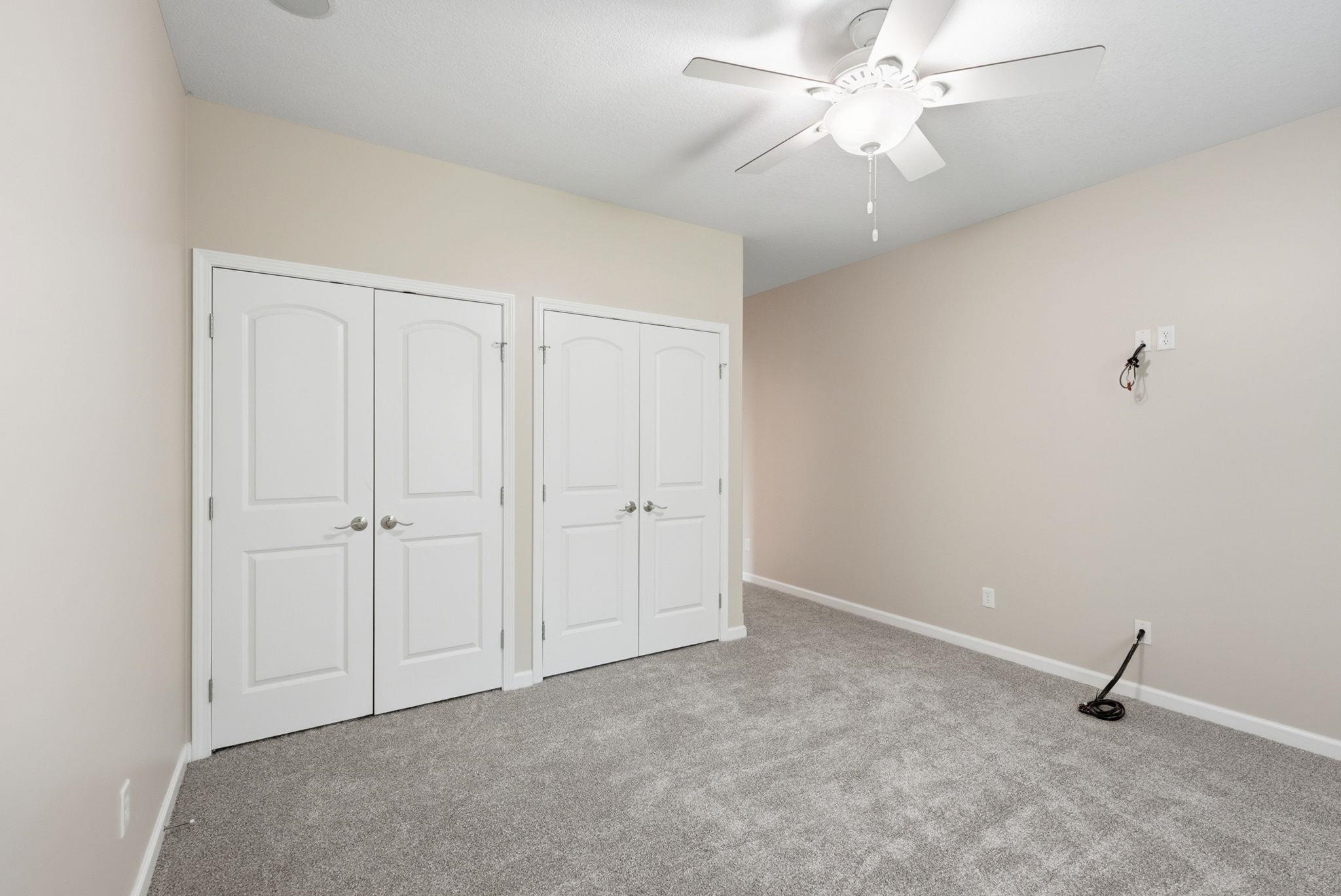 Neutral-toned room featuring a ceiling fan with integrated lighting, two sets of white double-door closets, and soft gray carpeting