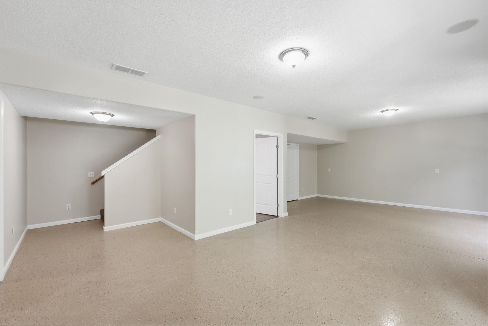 Spacious finished lower level featuring light neutral wall tones, flush-mounted ceiling lighting, and durable flooring