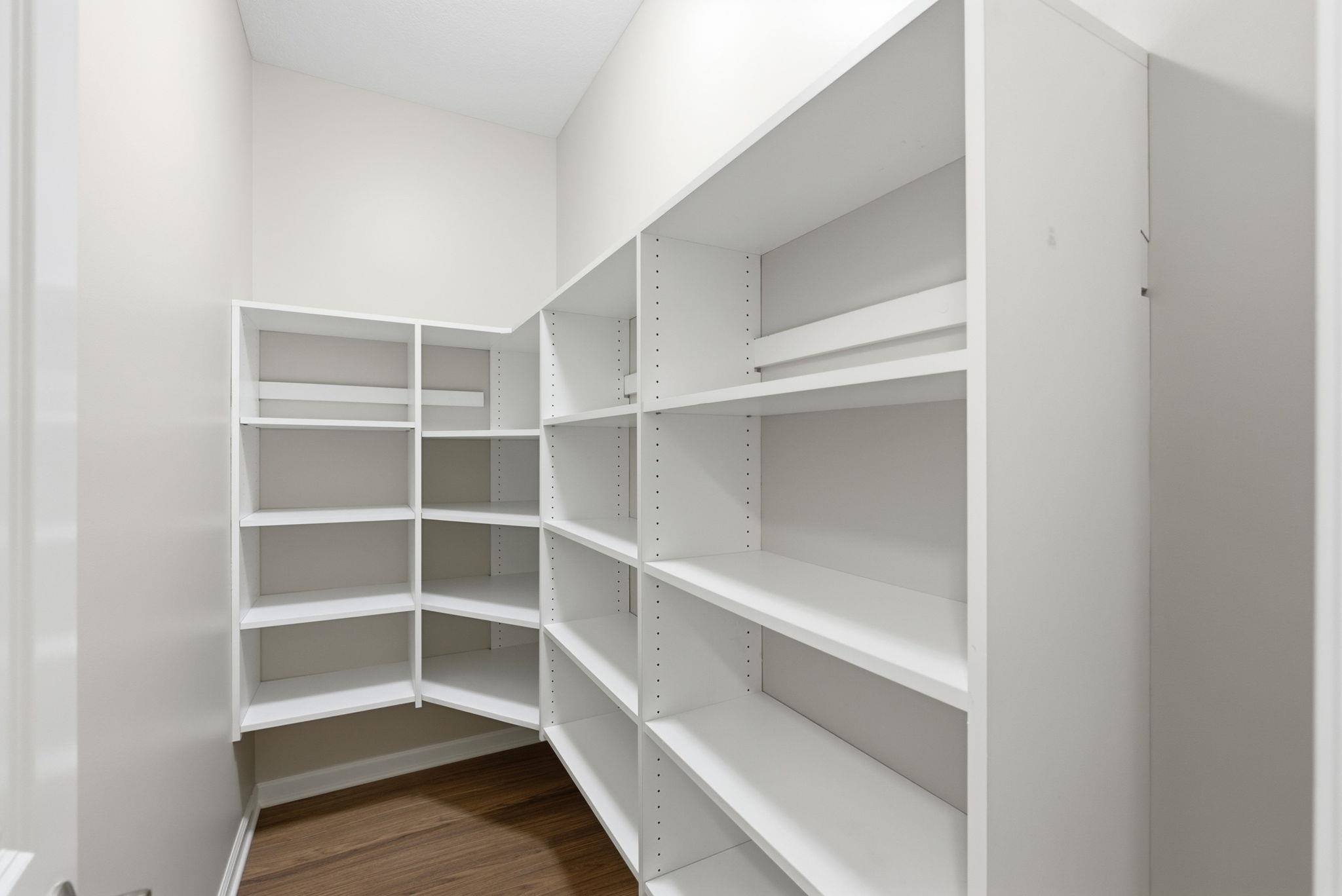 Expansive walk-in pantry featuring white shelving, high ceilings, and wood-finish flooring