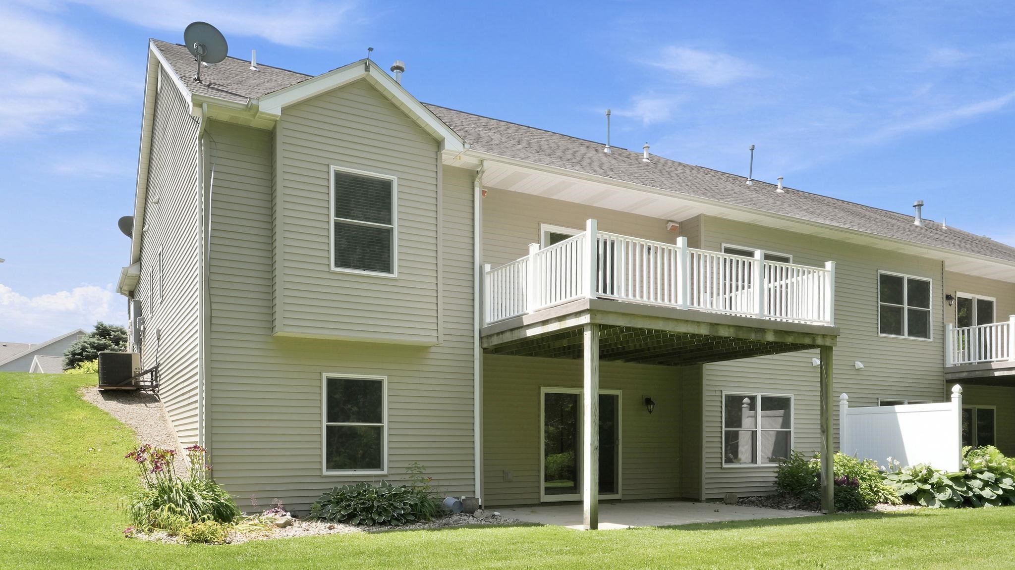 Rear exterior featuring light-colored siding, a second-story deck with white railing, and a ground-level patio