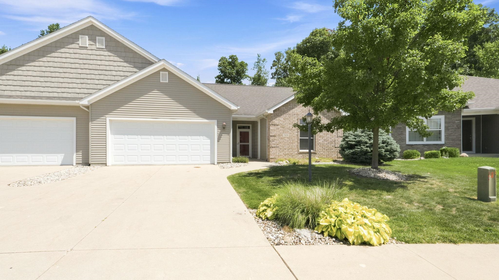 Exterior featuring light-toned siding, a two-car garage, a covered entry with a red door, and brick accents