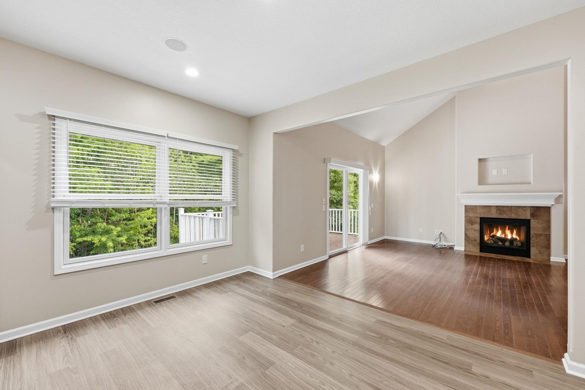 Bright living area featuring wood-finish flooring, a contemporary gas fireplace with tile surround, a vaulted ceiling, and sliding glass doors opening to a deck