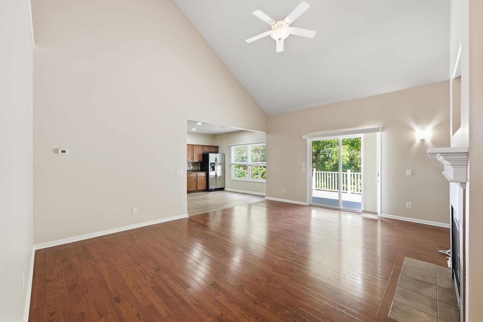 Spacious living area featuring wood-finish flooring, a vaulted ceiling with a ceiling fan, and light-toned walls