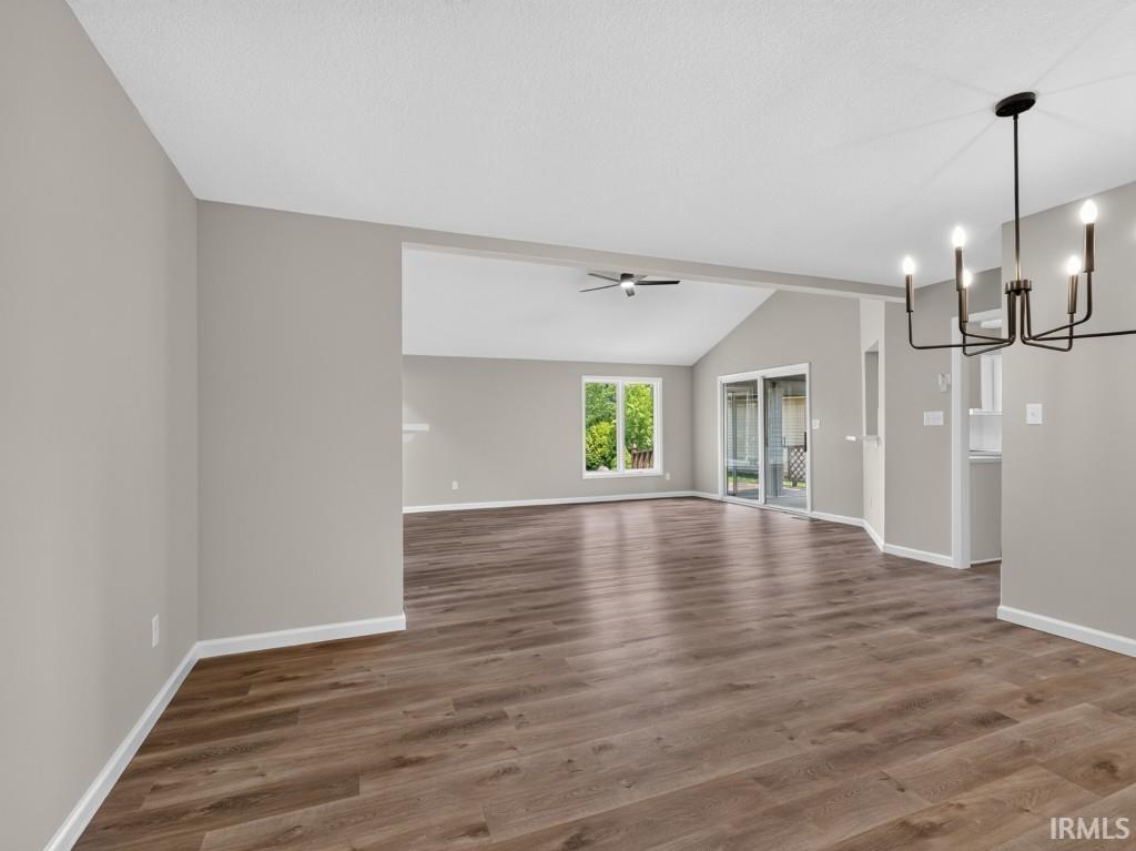 Expansive open-concept living area featuring wood-finish flooring, vaulted ceilings, and a modern black chandelier