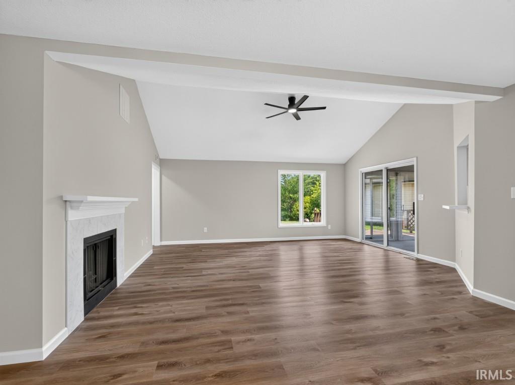 Spacious living area featuring wood-finish flooring, a white mantel fireplace with a black firebox, and a vaulted ceiling with a modern ceiling fan