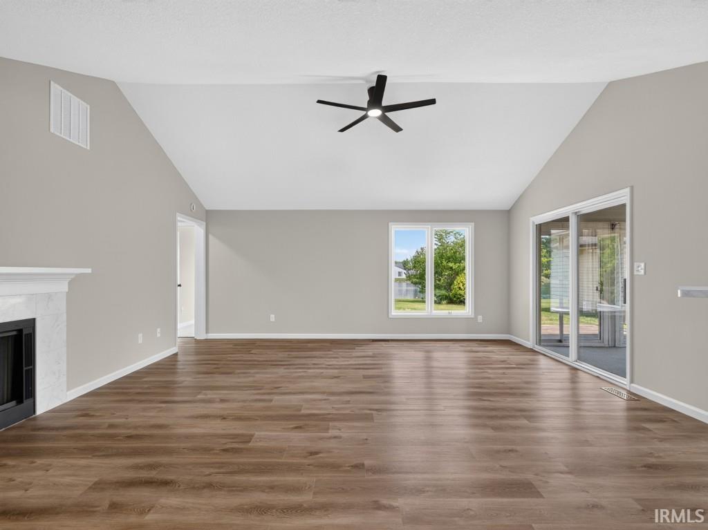 Vaulted ceiling living area featuring wood-finish flooring, a white fireplace with dark firebox, a ceiling fan, a double window, and sliding glass doors
