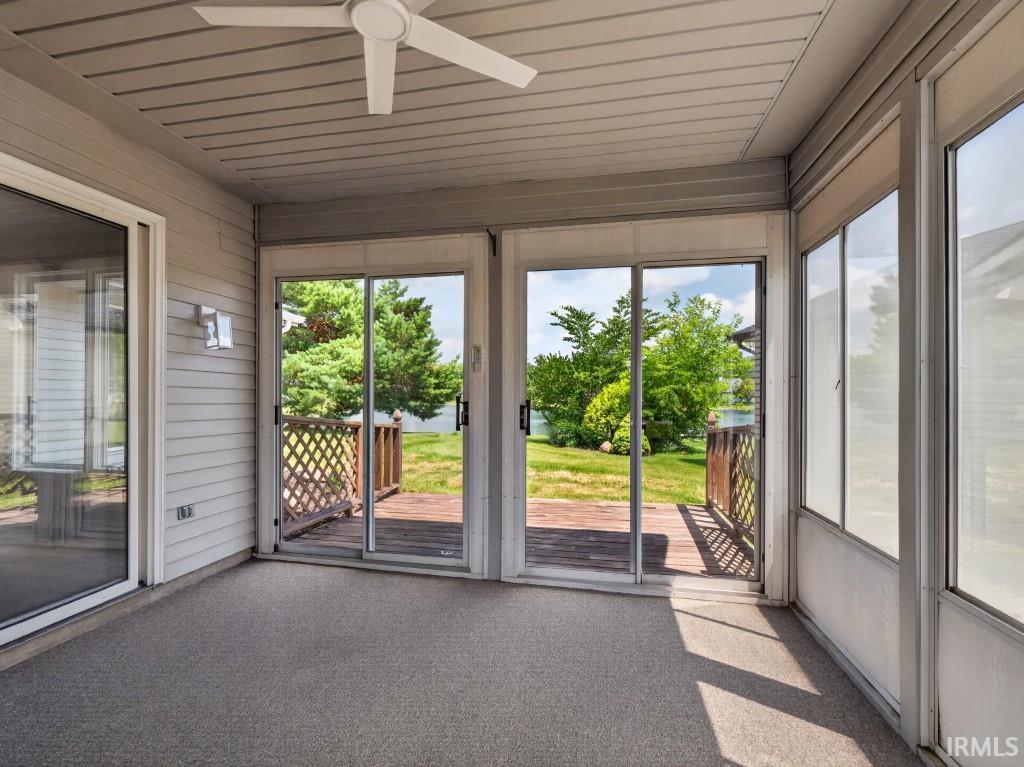 Screened porch featuring a textured floor, ceiling fan, and sliding glass doors opening to a wooden deck and exterior landscaping