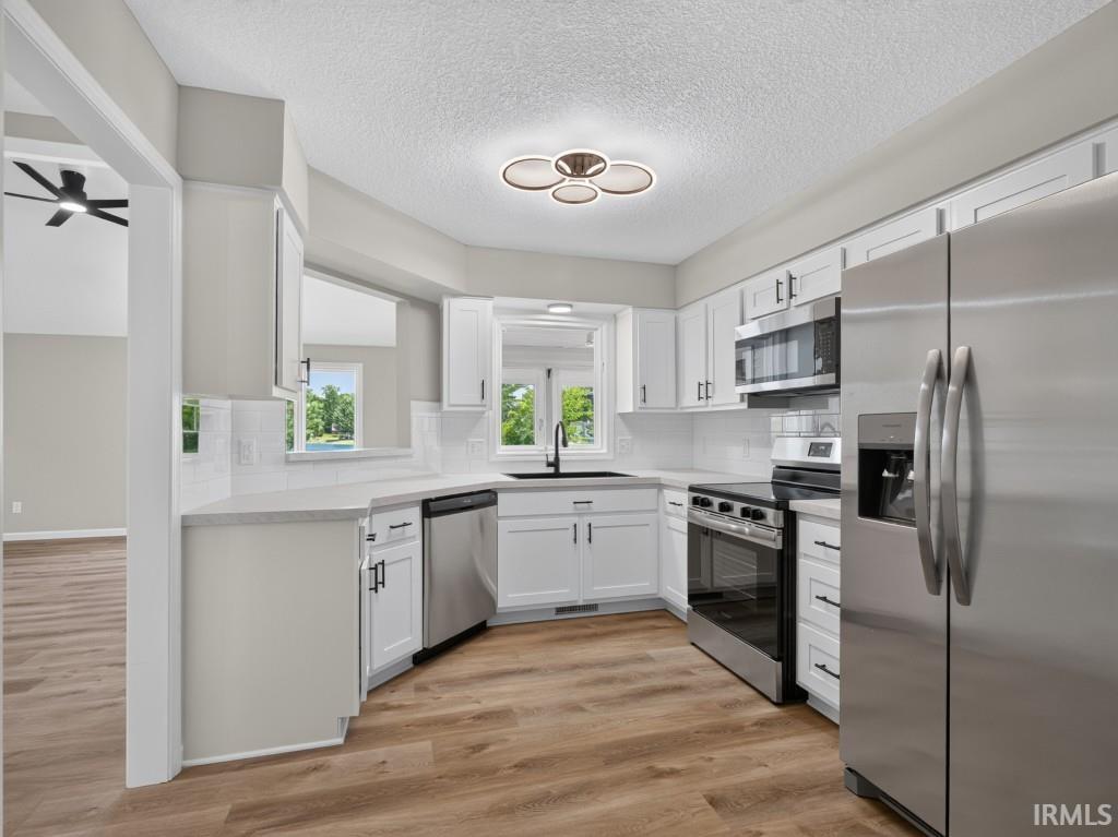 Modern kitchen featuring wood-finish flooring, white cabinetry with black hardware, stainless steel appliances, white subway tile backsplash, and light-colored countertops