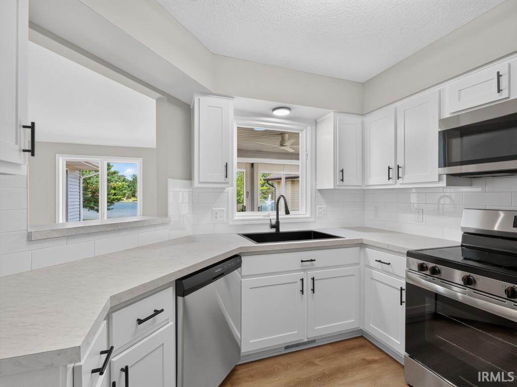 Kitchen featuring white cabinetry, light-toned countertops, a white subway tile backsplash, and stainless steel appliances