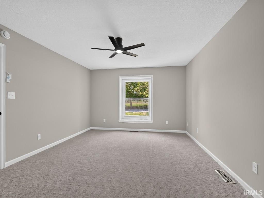Neutral-toned room featuring a modern black ceiling fan with integrated lighting, a single window, and plush gray carpeting