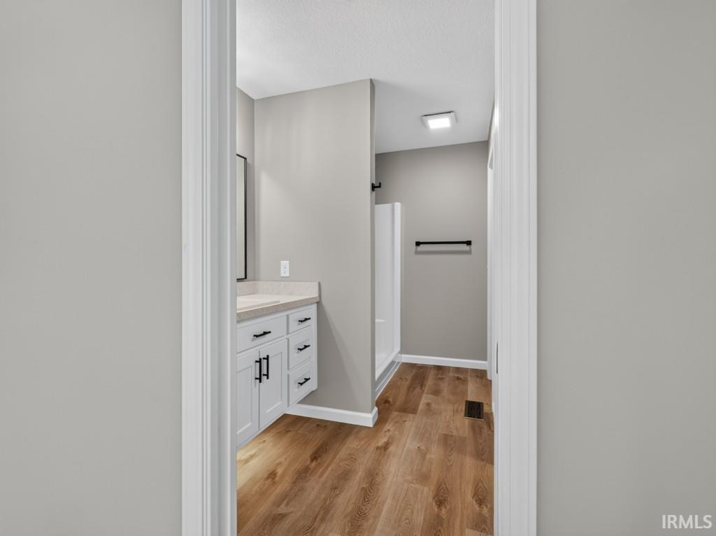 Bathroom featuring a white vanity with black hardware, a light-toned countertop, wood-finish flooring, and a shower stall