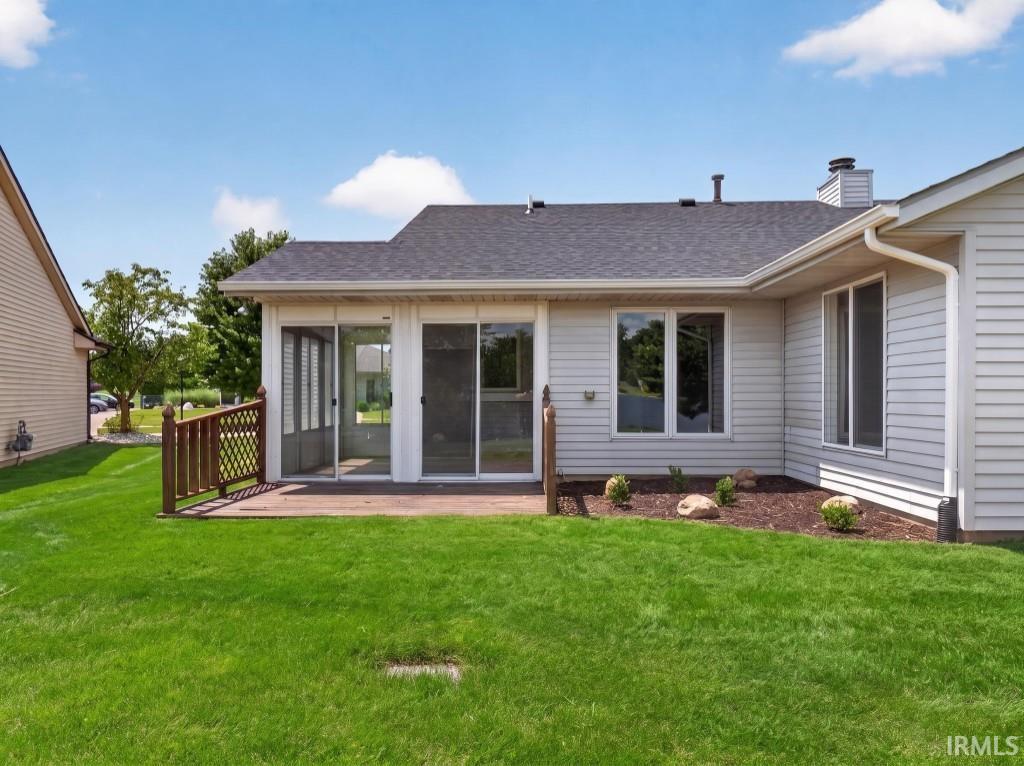 Spacious backyard featuring a wooden deck, screened-in porch with sliding glass doors, and a manicured lawn