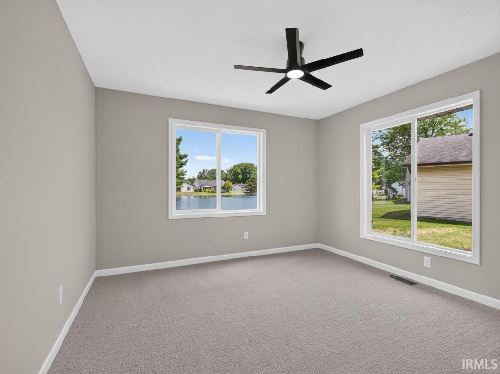 Bright interior space featuring two large windows, a ceiling fan with integrated lighting, neutral wall tones, and carpet flooring