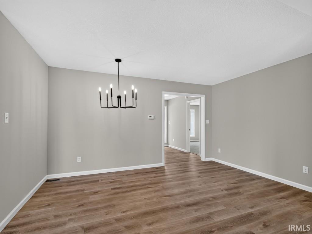 Spacious interior room featuring wood-finish flooring, light gray wall tones, and white baseboards