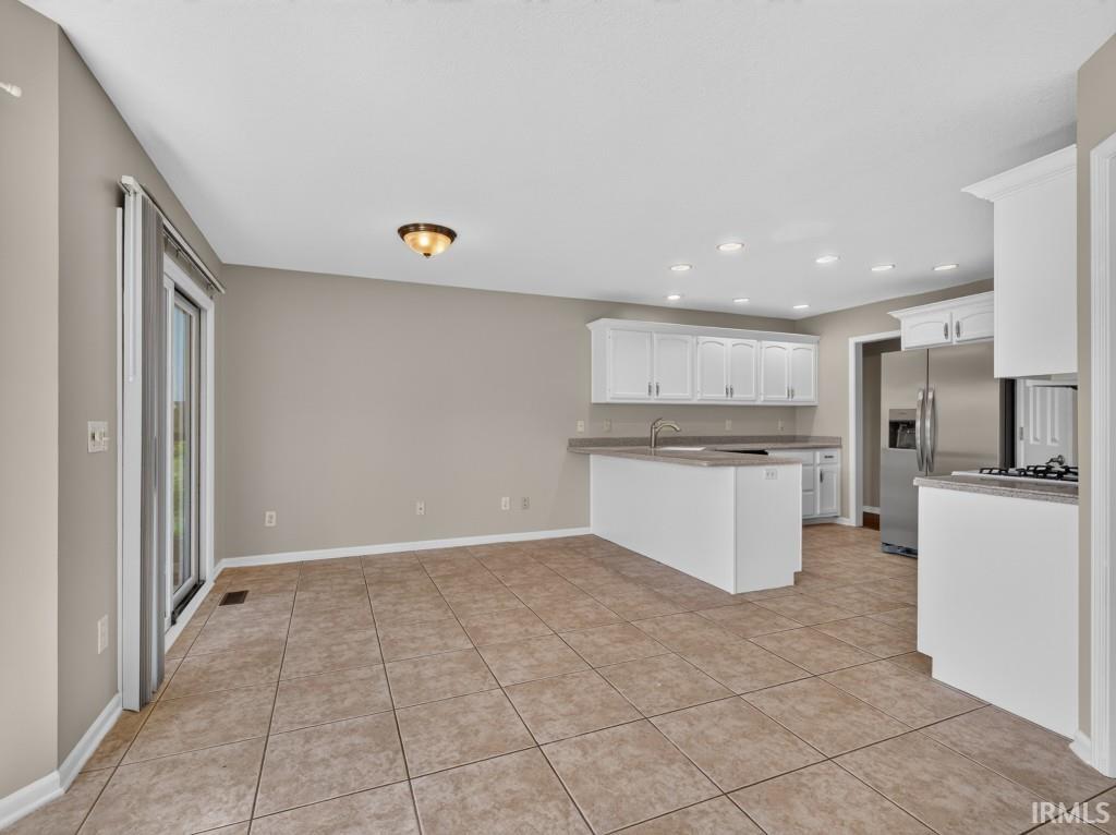 Open-concept kitchen and dining area featuring ceramic tile flooring, white cabinetry, recessed lighting, and a stainless steel refrigerator