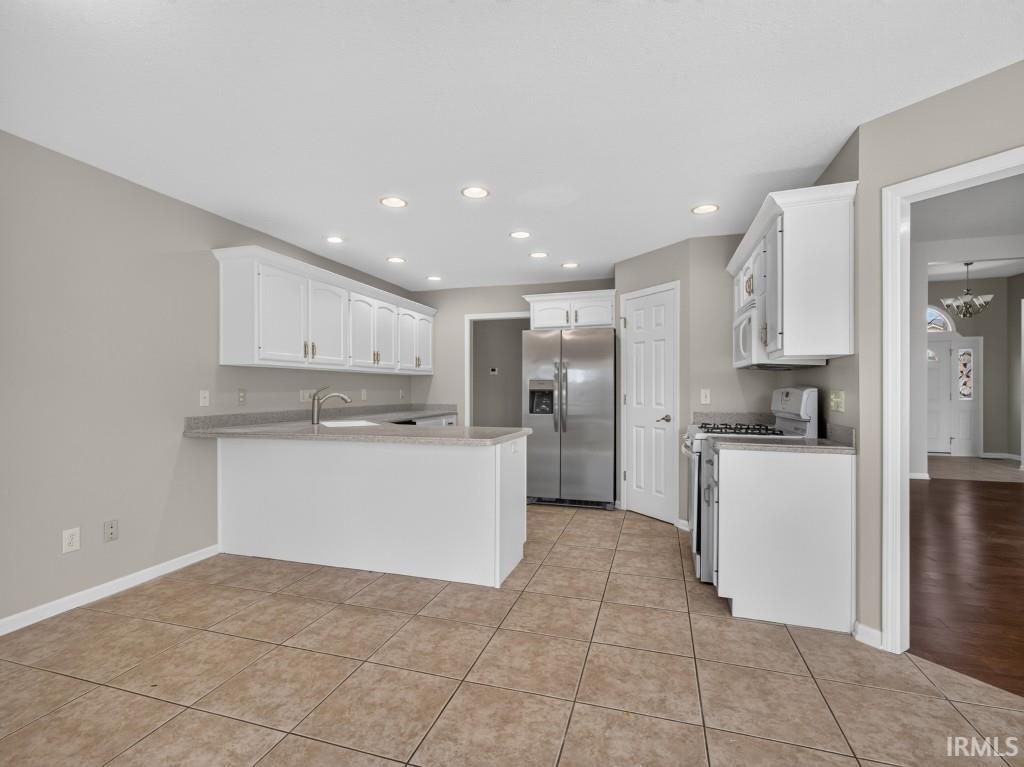 Kitchen featuring white cabinetry, stainless steel appliances, recessed lighting, tile flooring, and a breakfast bar with a sink