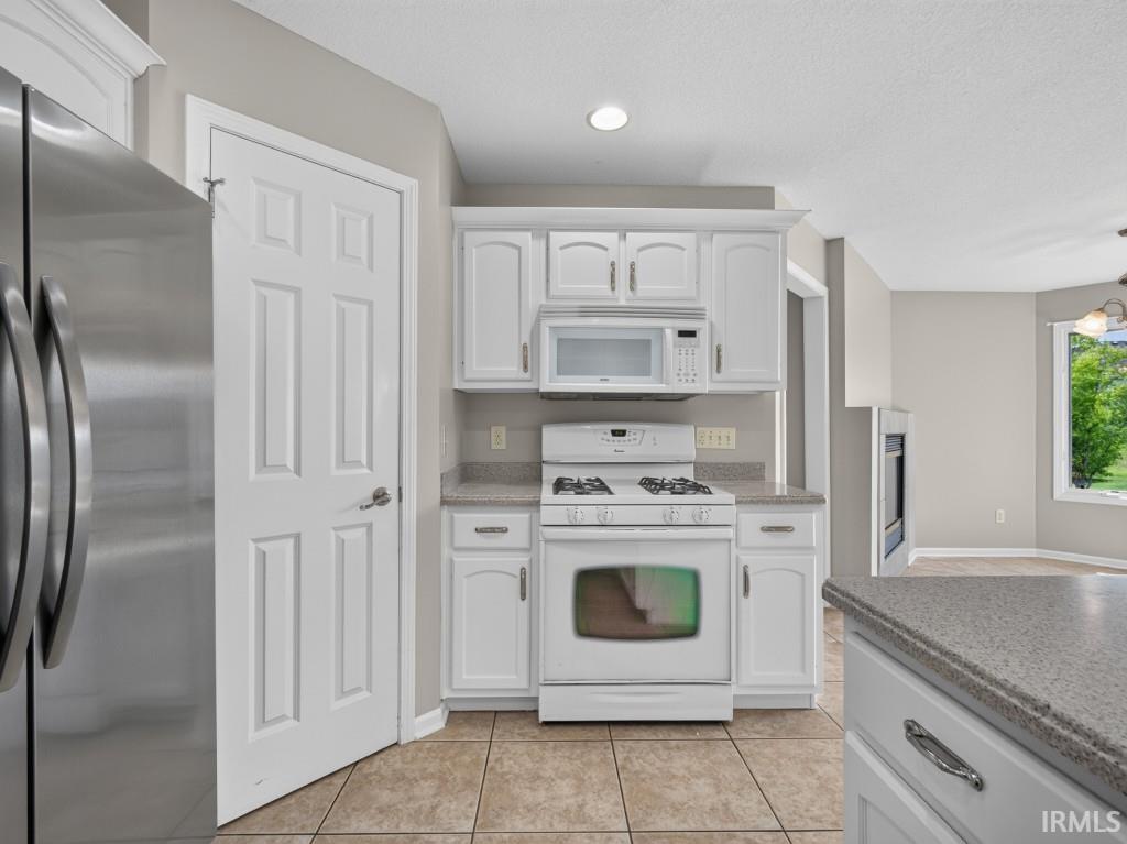 Kitchen featuring white cabinetry, light-colored countertops, tile flooring, a stainless steel refrigerator, and a white oven with a microwave above