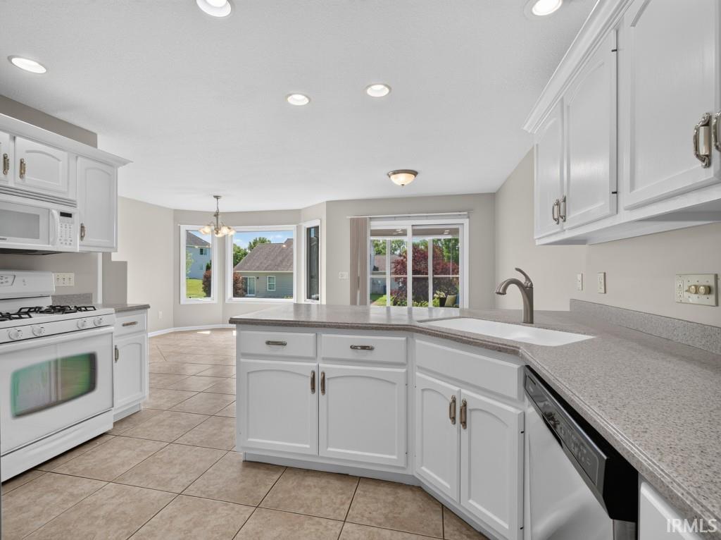 Kitchen featuring white cabinetry, light-toned countertops, a stainless steel sink with a gooseneck faucet, a built-in dishwasher, and recessed lighting