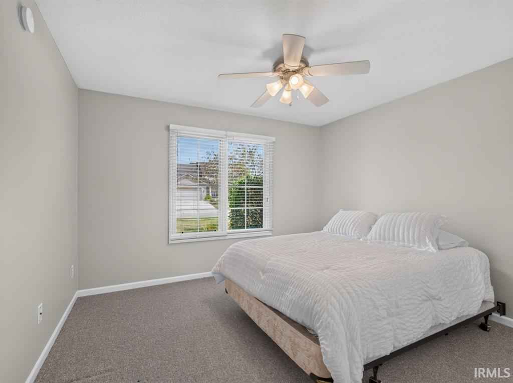 Neutral wall tones, gray carpeting, a window with blinds, a ceiling fan with integrated lighting, and a smoke detector