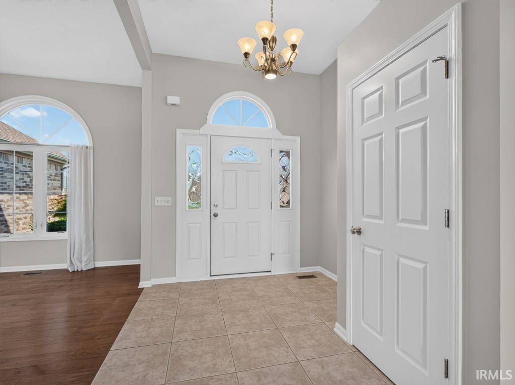 Entryway featuring ceramic tile flooring, a chandelier, and a white paneled door with decorative sidelights and an arched transom