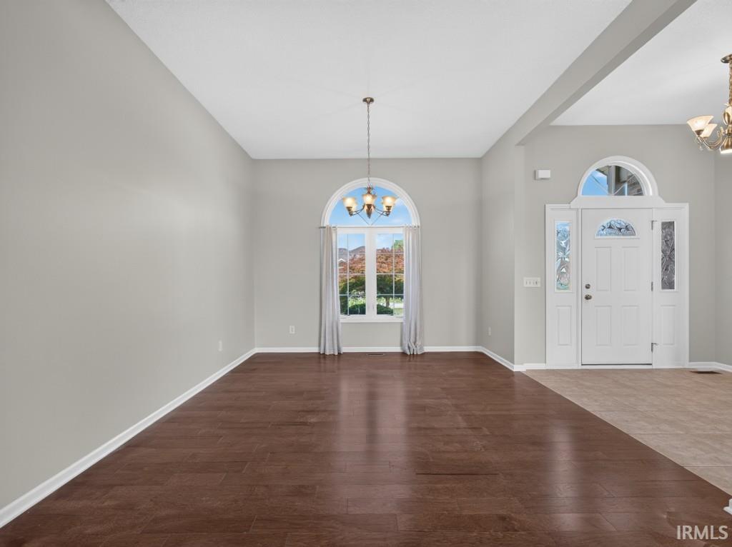 Spacious room featuring wood-finish flooring, a large arched window with a transom, and a contemporary chandelier