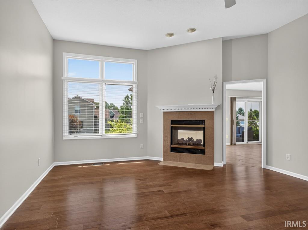 Living area featuring wood-finish flooring, a corner fireplace with a stone surround and white mantel, and a large multi-pane window