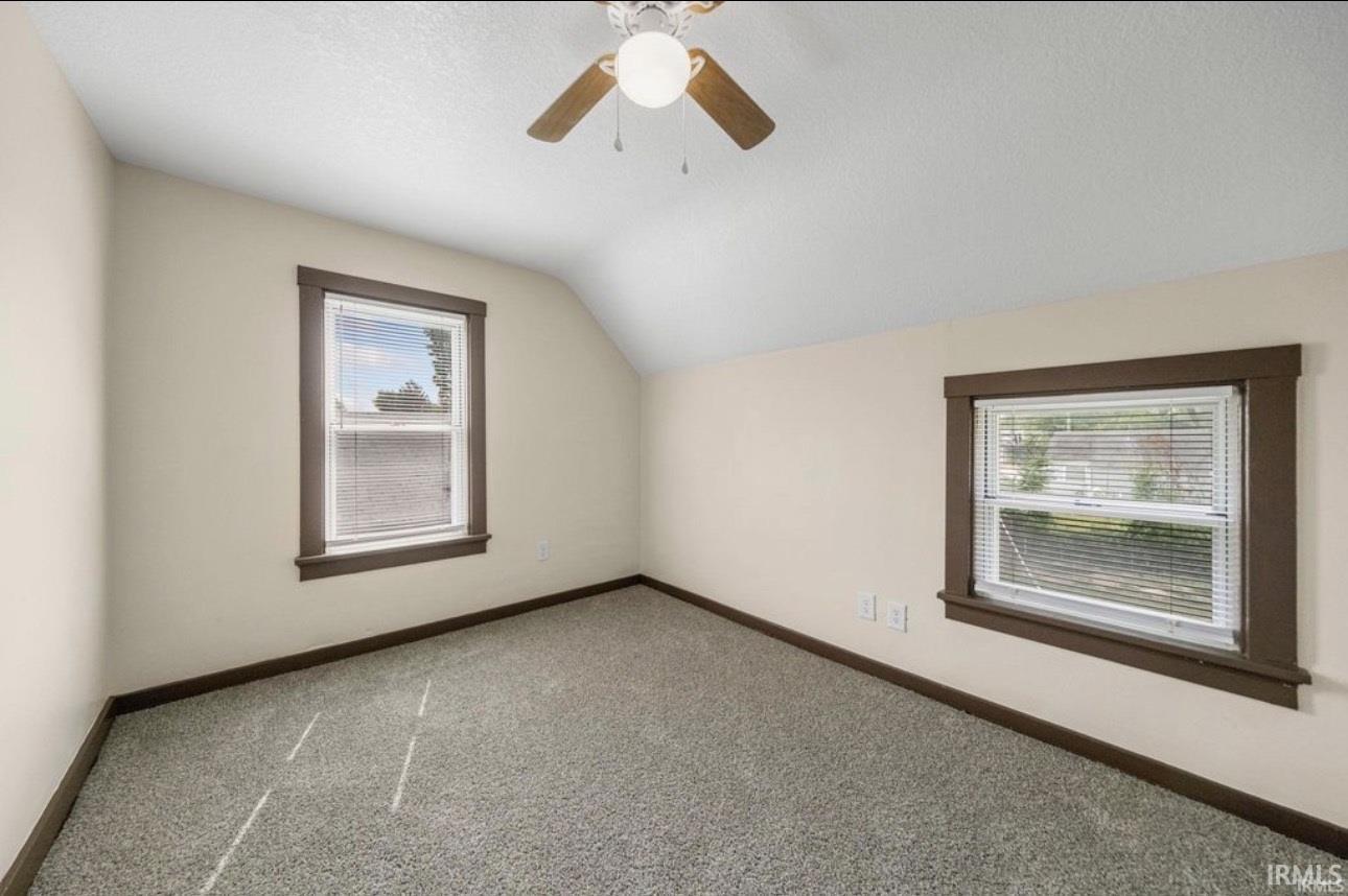 Carpeted room featuring two windows with dark wood trim, a ceiling fan with integrated lighting, and neutral wall paint