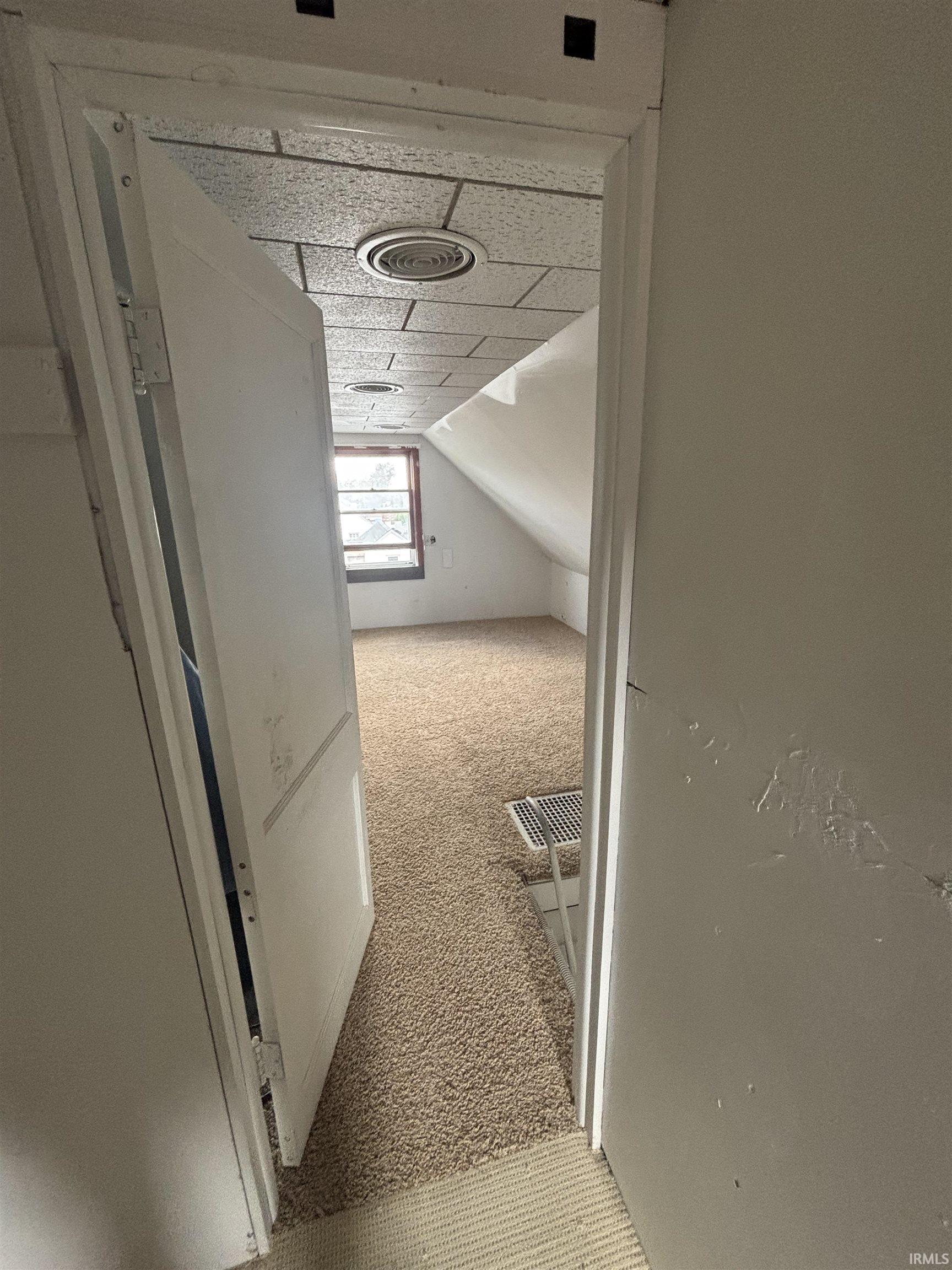 Carpeted room featuring an angled ceiling, recessed window, and acoustic tile ceiling with circular vents