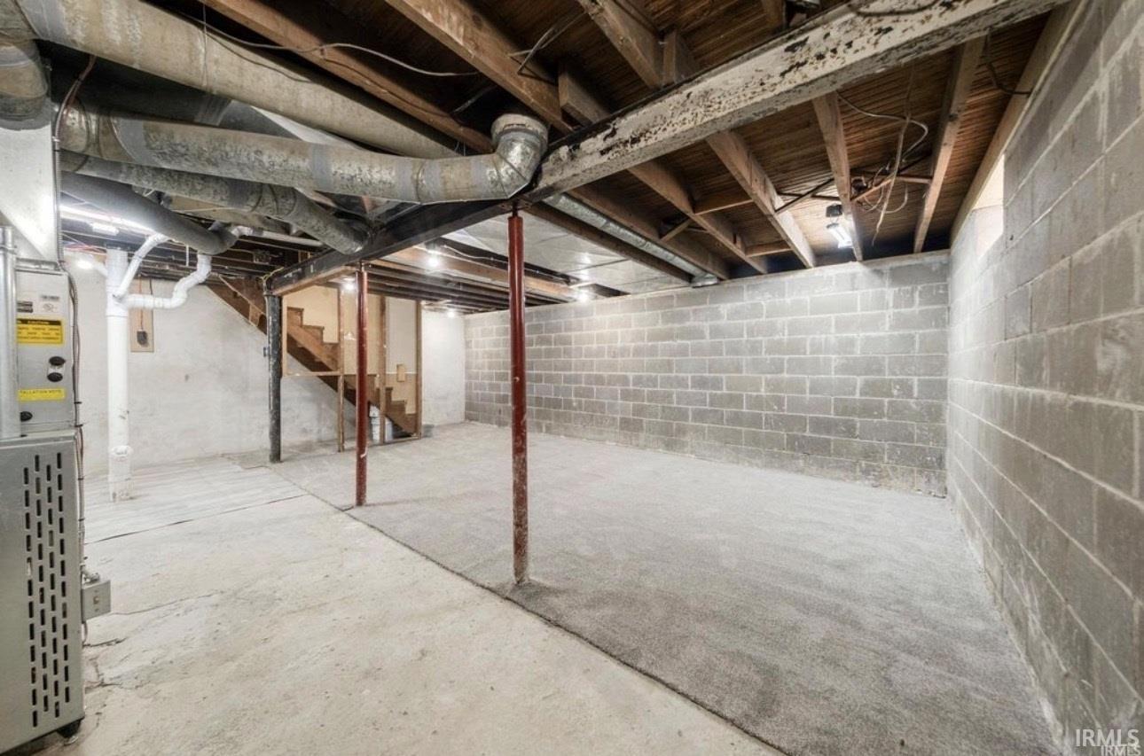 Unfinished basement space featuring exposed wood joists, concrete block walls, and a concrete floor