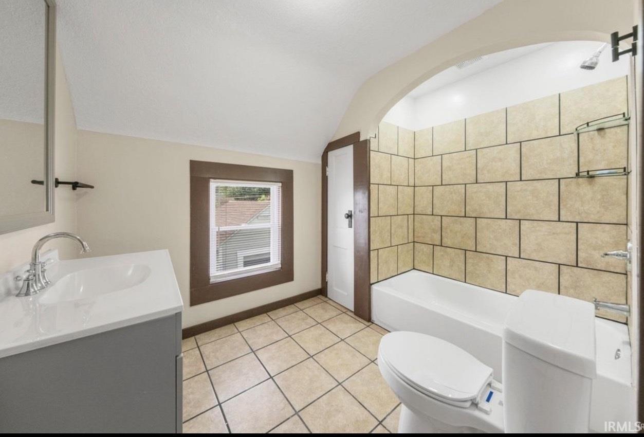 Bathroom featuring a single vanity with an integrated sink, a tiled floor, and a tub-shower combination with tiled surround