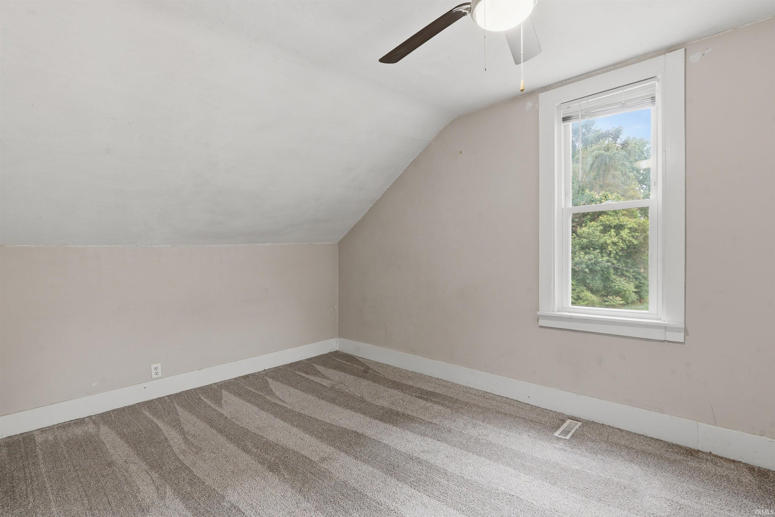 Room featuring sloped ceilings, a single window, a ceiling fan with integrated lighting, and patterned carpet flooring