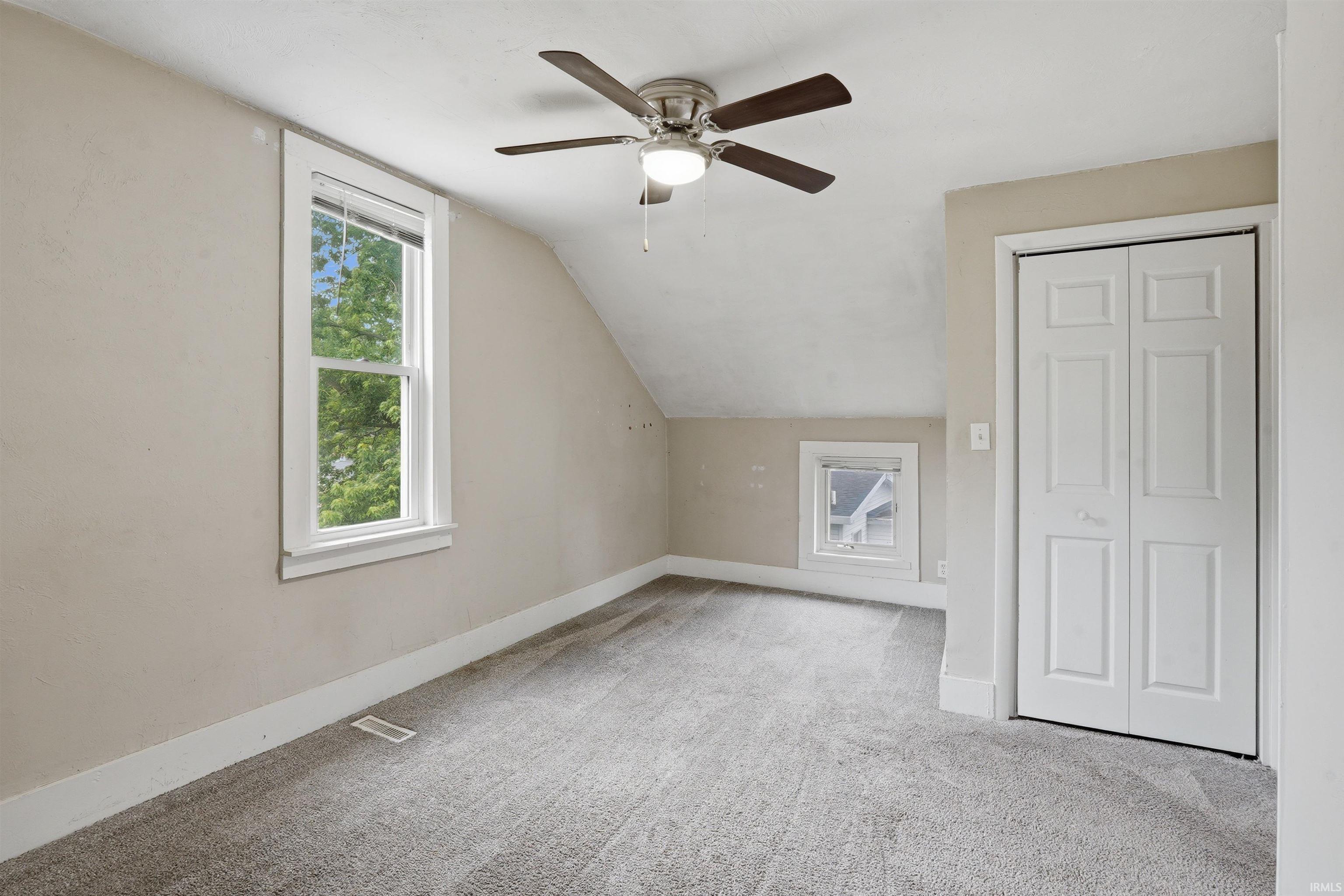 Carpeted room featuring a ceiling fan with integrated lighting, a double-hung window, a smaller fixed window, and a bi-fold closet door