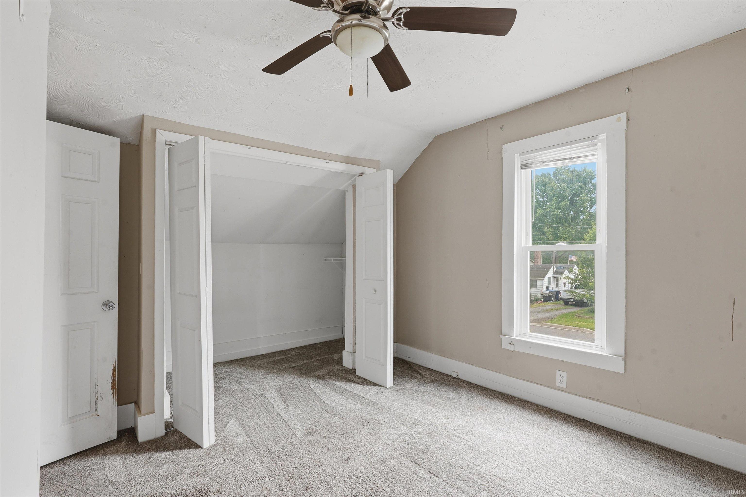 Carpeted room featuring a ceiling fan with integrated lighting, a window with white trim, and a bi-fold closet