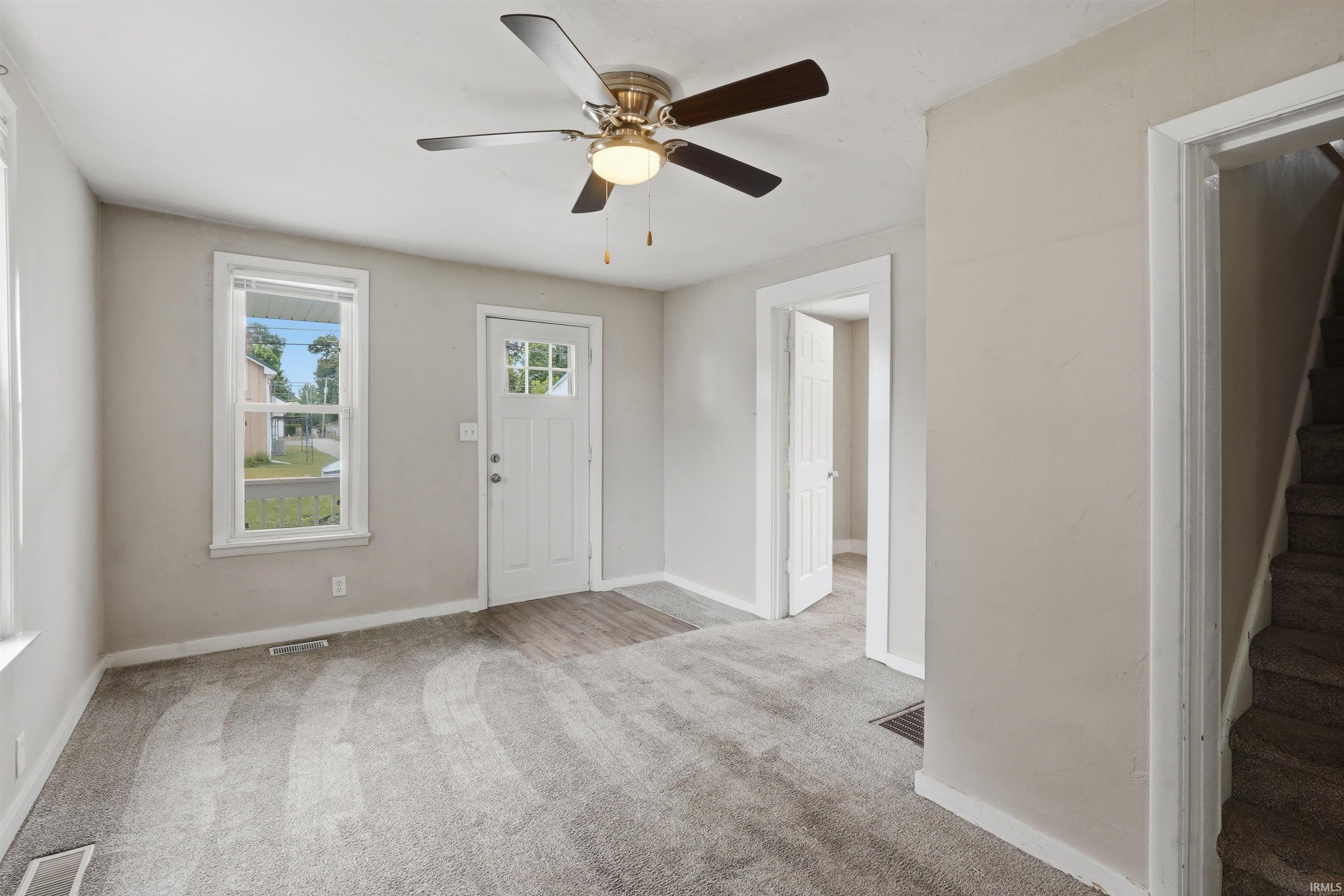 Living area featuring light gray wall paint, a ceiling fan with integrated lighting, and neutral carpeting