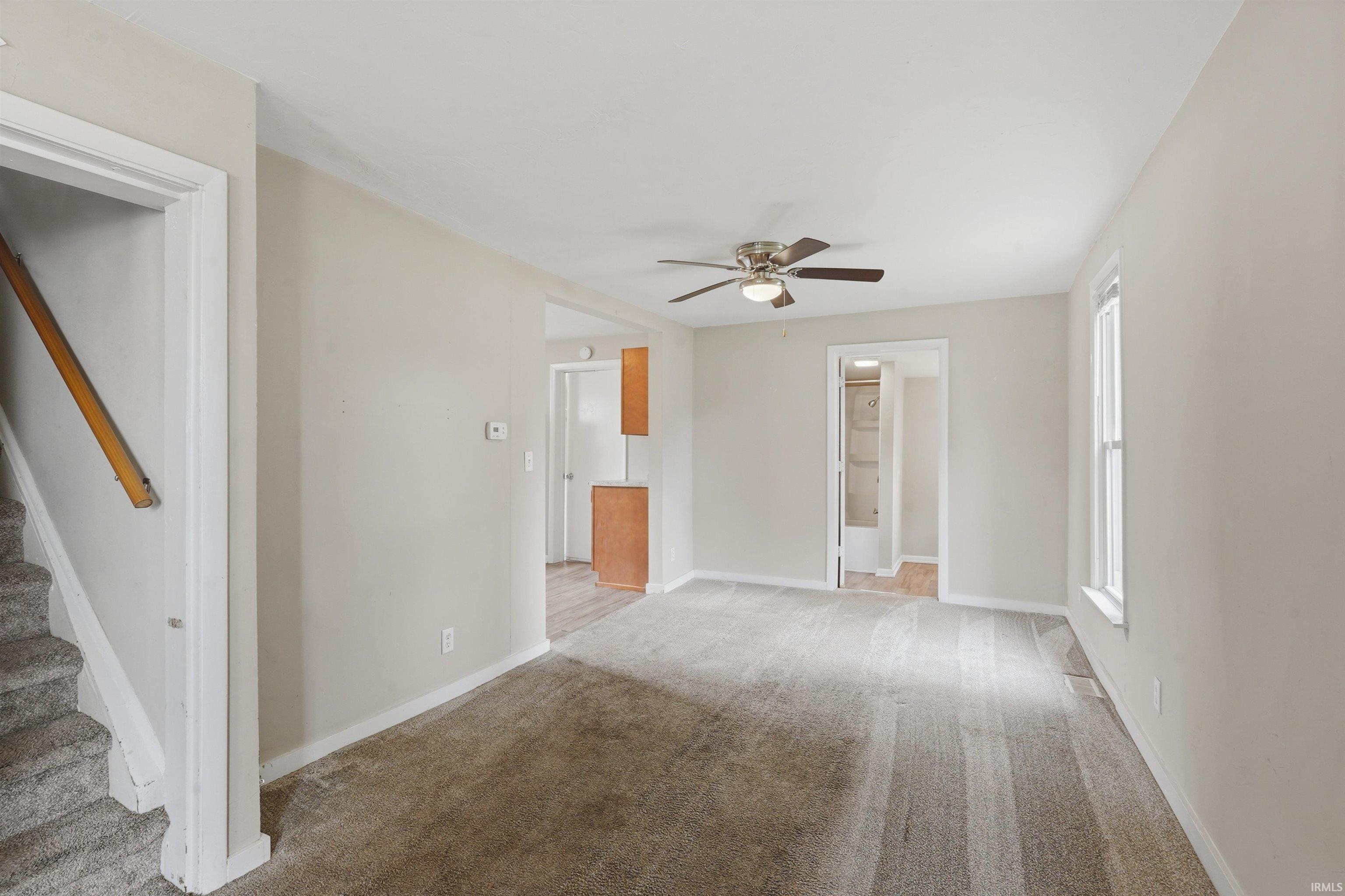 Spacious room featuring neutral paint, soft carpeting, a ceiling fan, and natural light from a window
