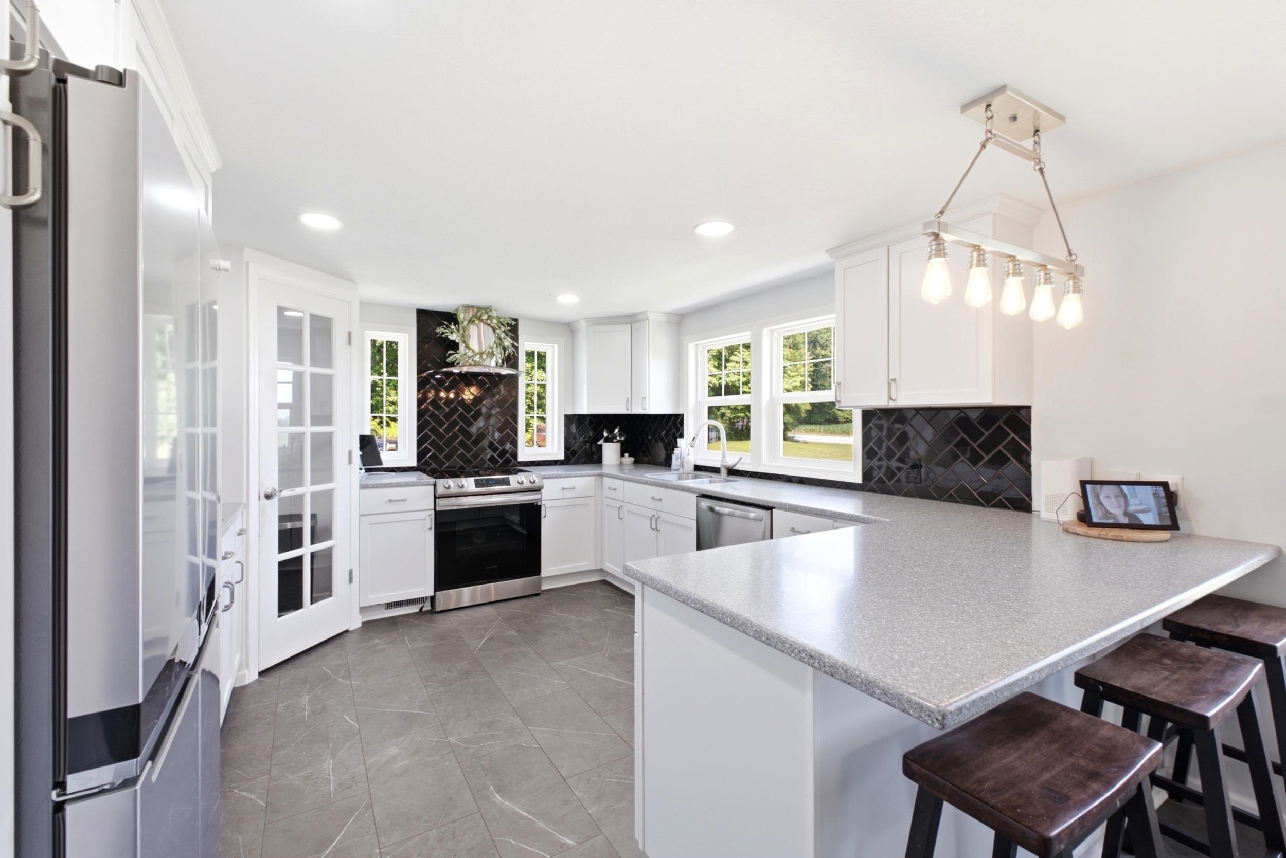 Modern kitchen featuring white cabinetry, a black herringbone tile backsplash, stainless steel appliances, a bar-height countertop, and recessed lighting