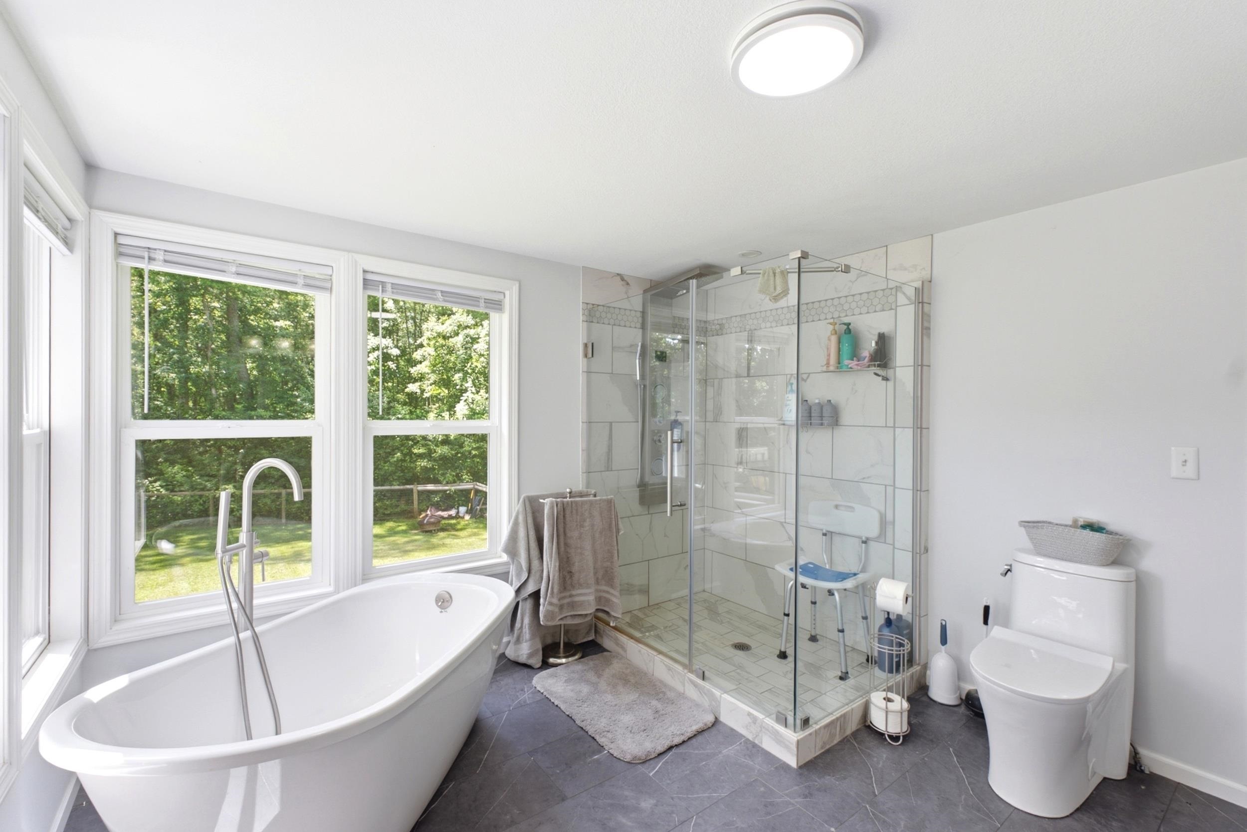 Bathroom featuring a freestanding tub with floor-mounted faucet, a glass-enclosed shower with tiled walls, multiple windows, and dark-toned flooring
