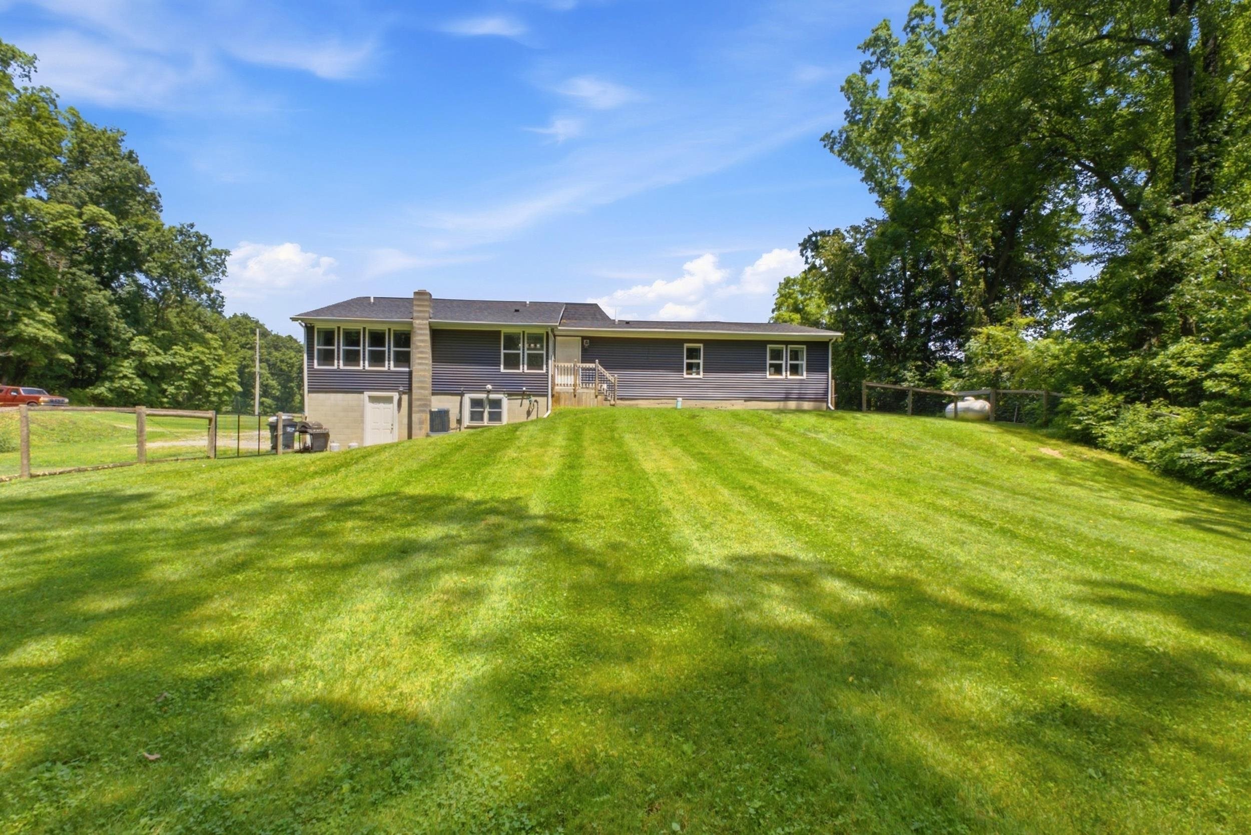 Expansive sloped lawn with mature perimeter trees and a fenced boundary