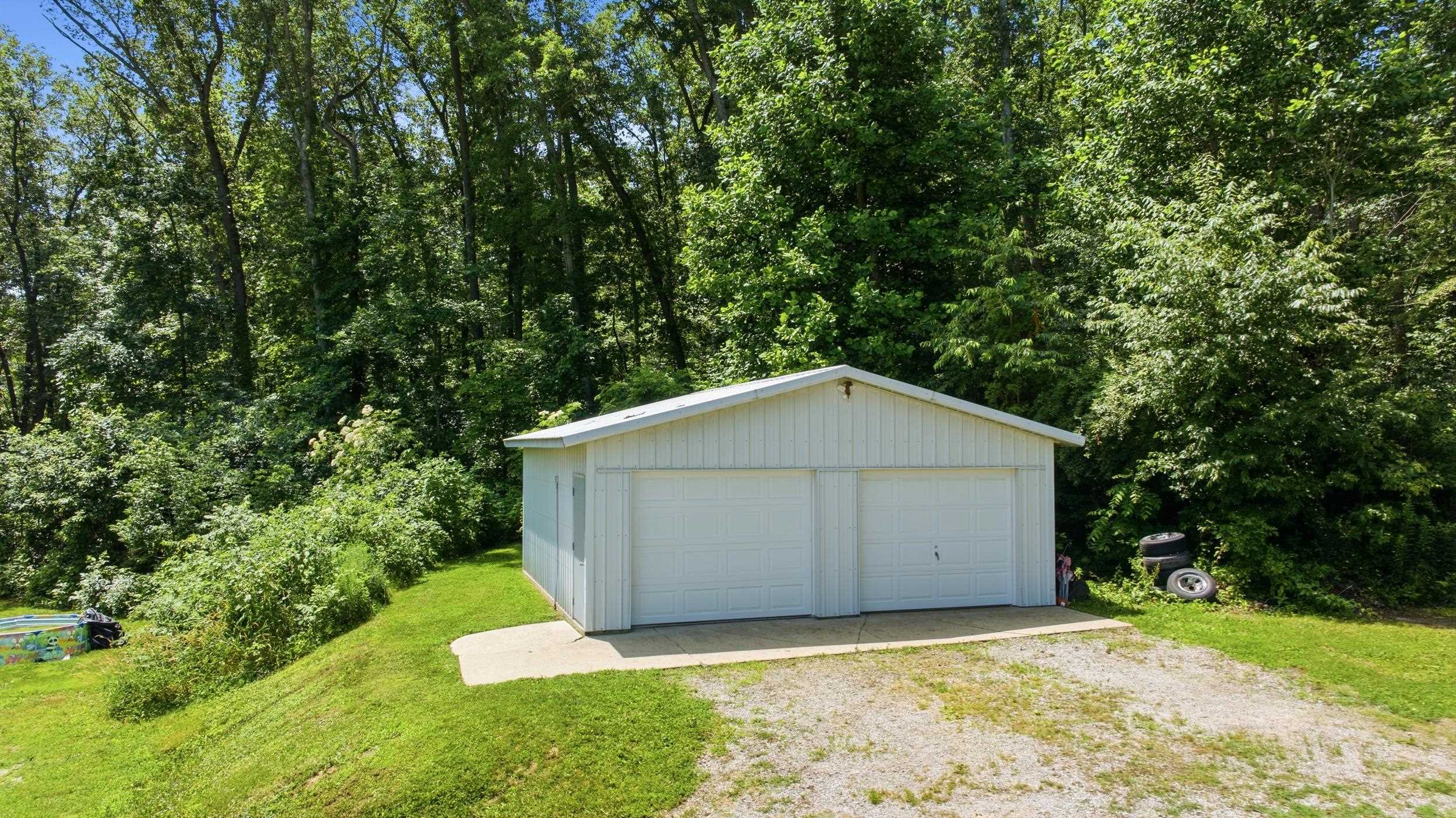 Detached garage with two roll-up doors, white vertical siding, and a gabled roof